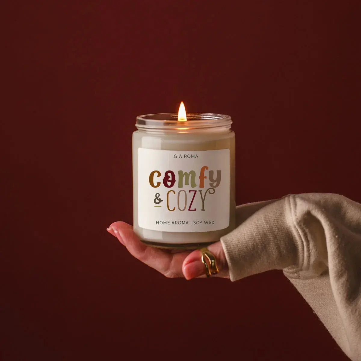 Hand holding a lit candle labeled 'Comfy & Cozy' against a dark background