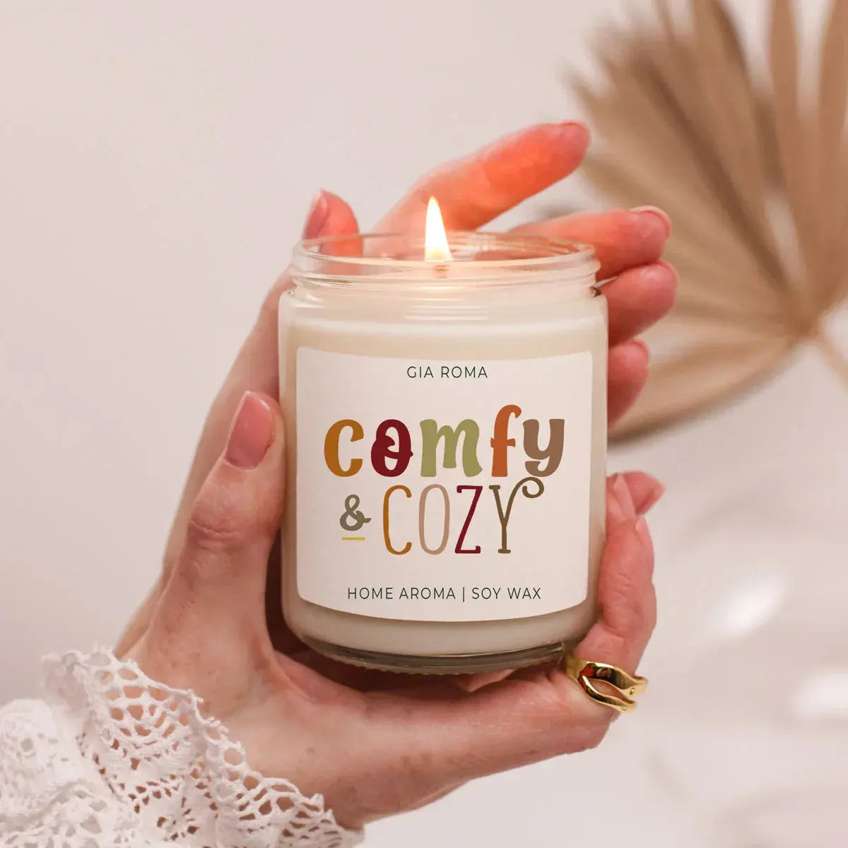 Hand holding a candle labeled 'comfy & cozy' with a blurred background