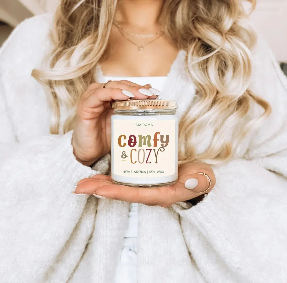 Person holding a 'Comfy & Cozy' candle with a soft focus background