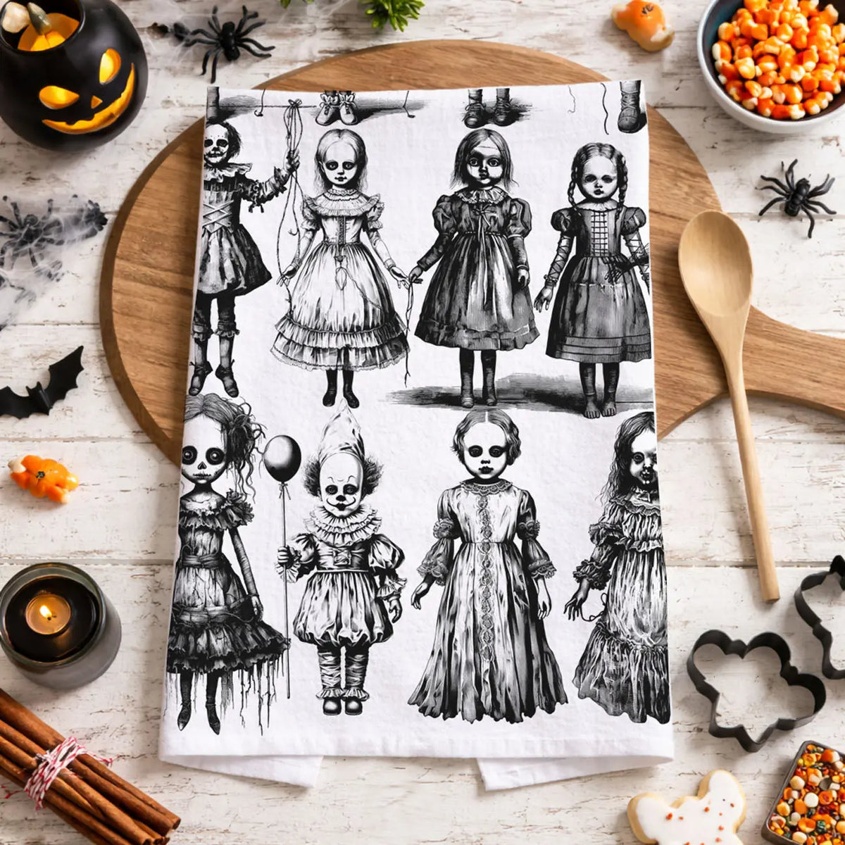 Halloween-themed kitchen towel with black and white illustrations of dolls on a wooden cutting board.