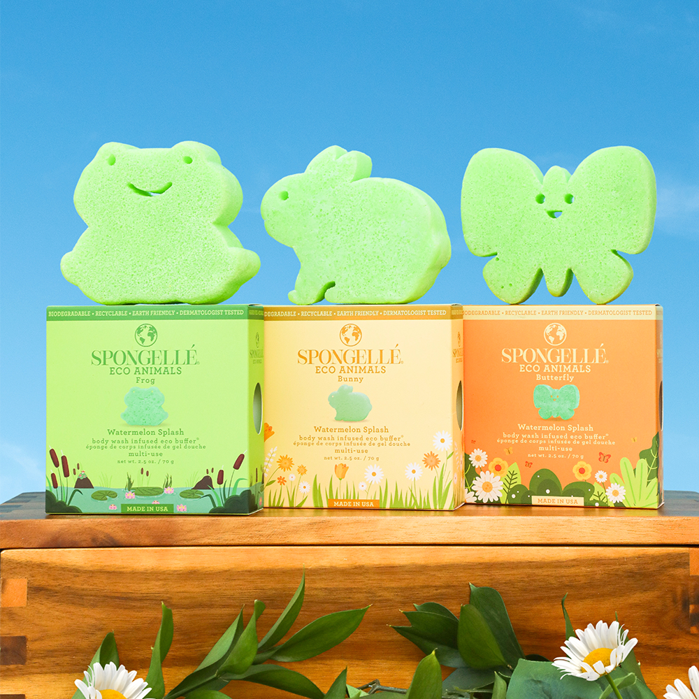 Three green animal-shaped sponges with packaging on a wooden surface against a blue sky.