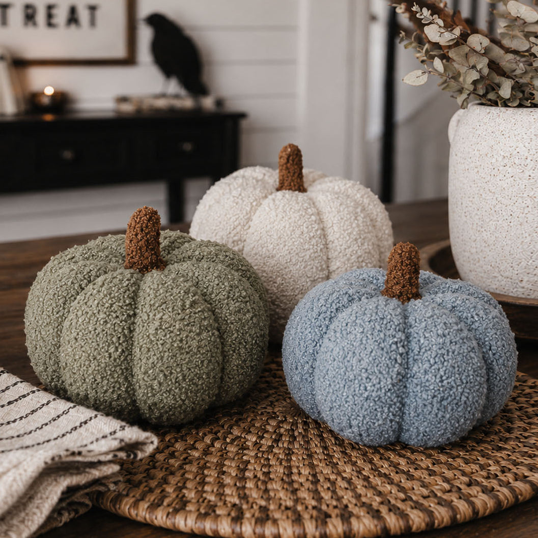 Three textured pumpkins in green, white, and blue on a woven mat with a blurred indoor background.
