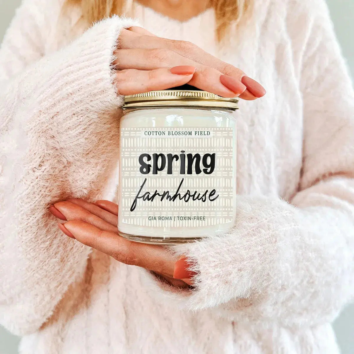 Person holding a 'Spring Cleaning' candle jar with a soft pink background