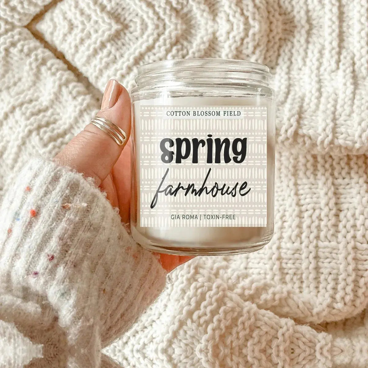 Candle labeled 'Spring Farmhouse' held against a textured beige background