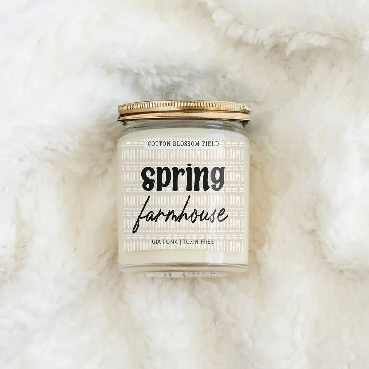 Candle jar labeled 'Spring Farmhouse' on a fluffy white surface