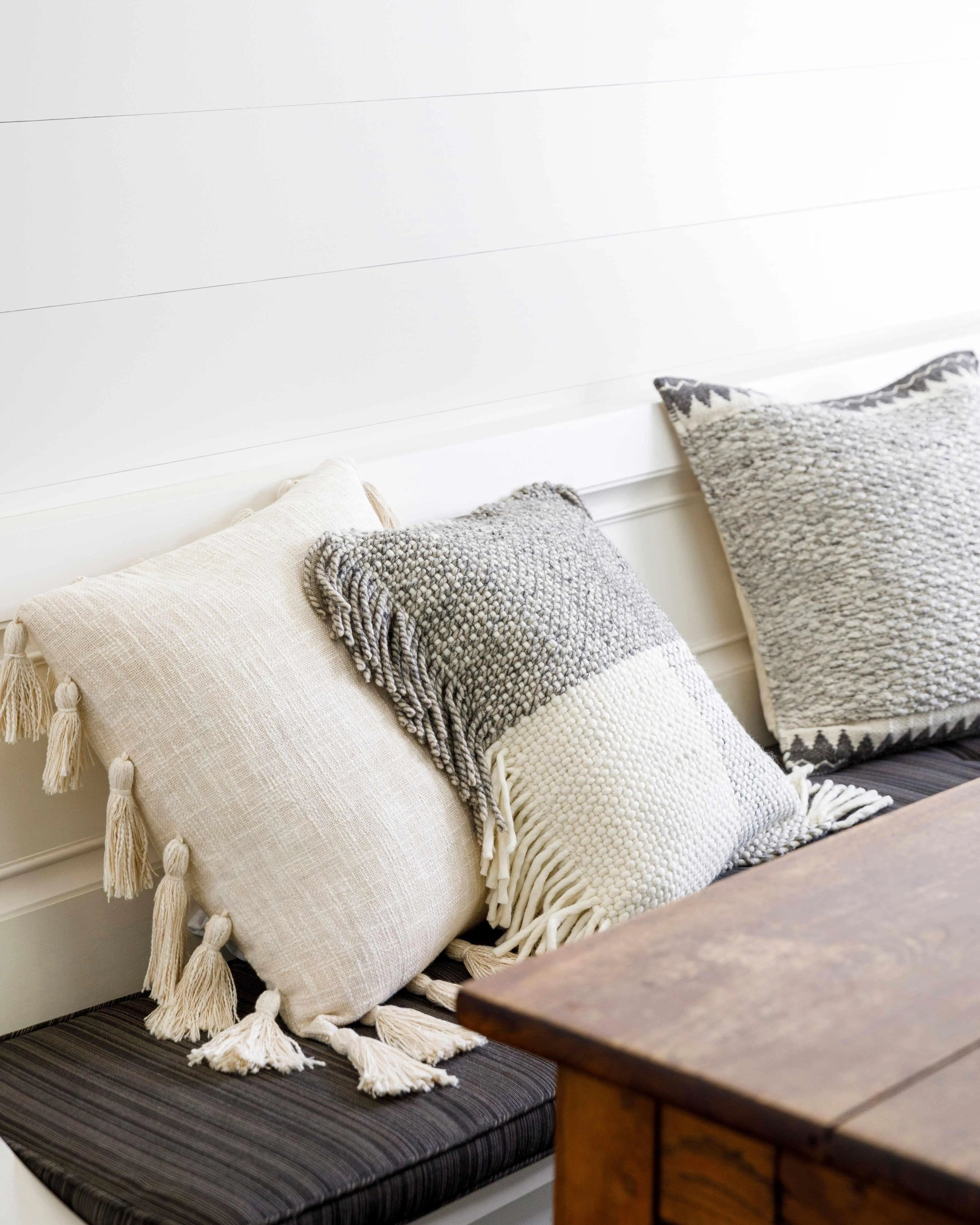 Cozy farmhouse throw pillows with tassels and woven textures on a cushioned bench, perfect for cottage style decor.