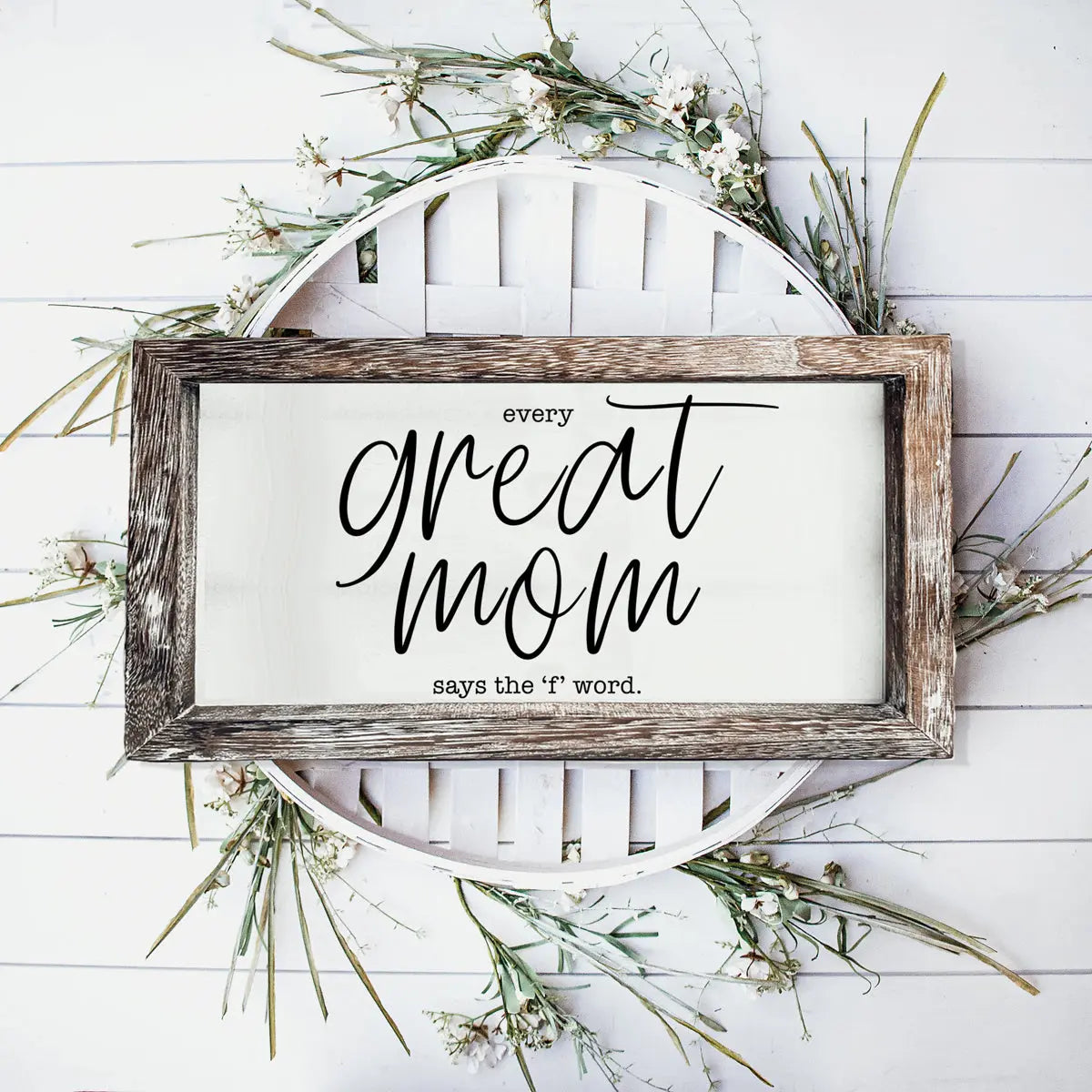 Decorative sign with text 'Every great mom says the f word' on a white background with greenery.