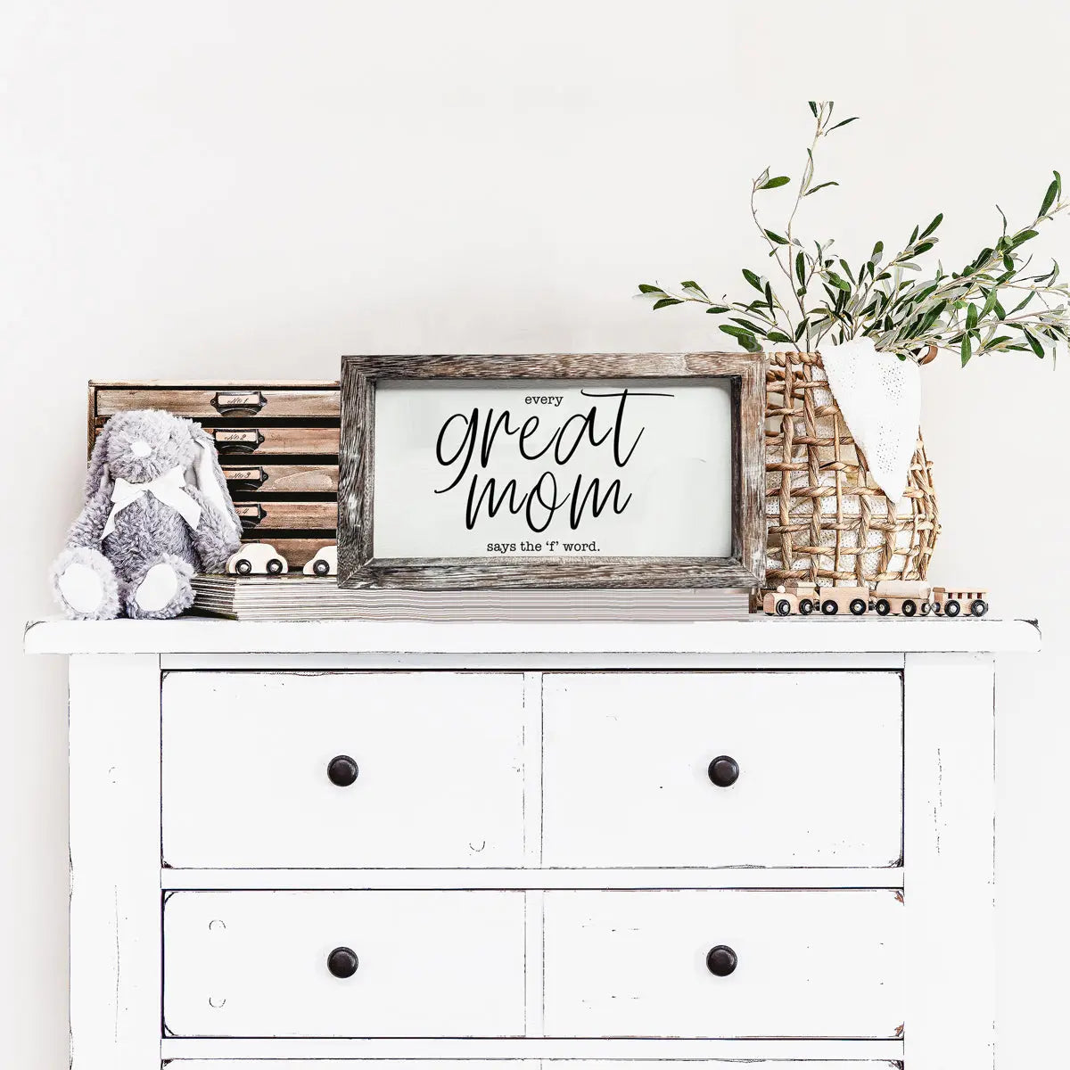 White dresser with decorative items including a framed sign, stuffed animal, and plant.