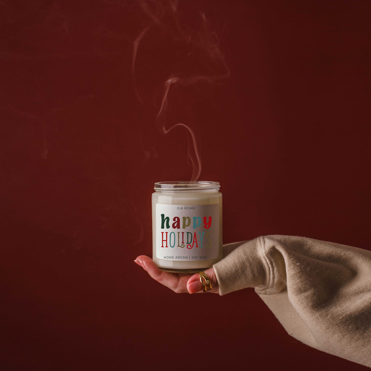 Hand holding a 'Comfy & Cozy' candle against a dark red background