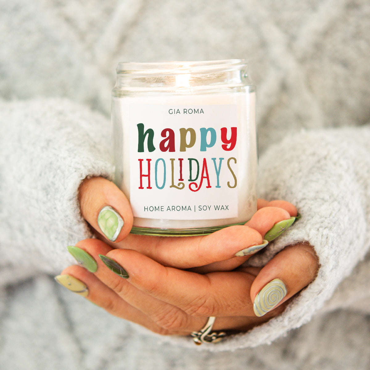 Hand holding a 'happy holidays' candle with a cozy background