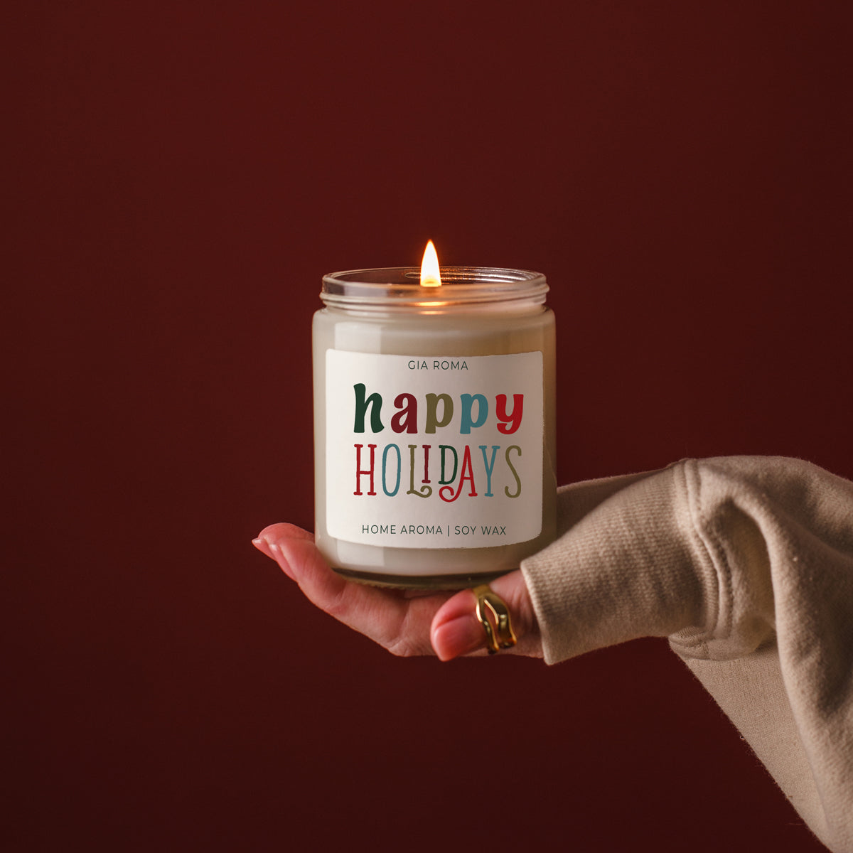 Hand holding a lit candle labeled 'happy holidays' against a dark background