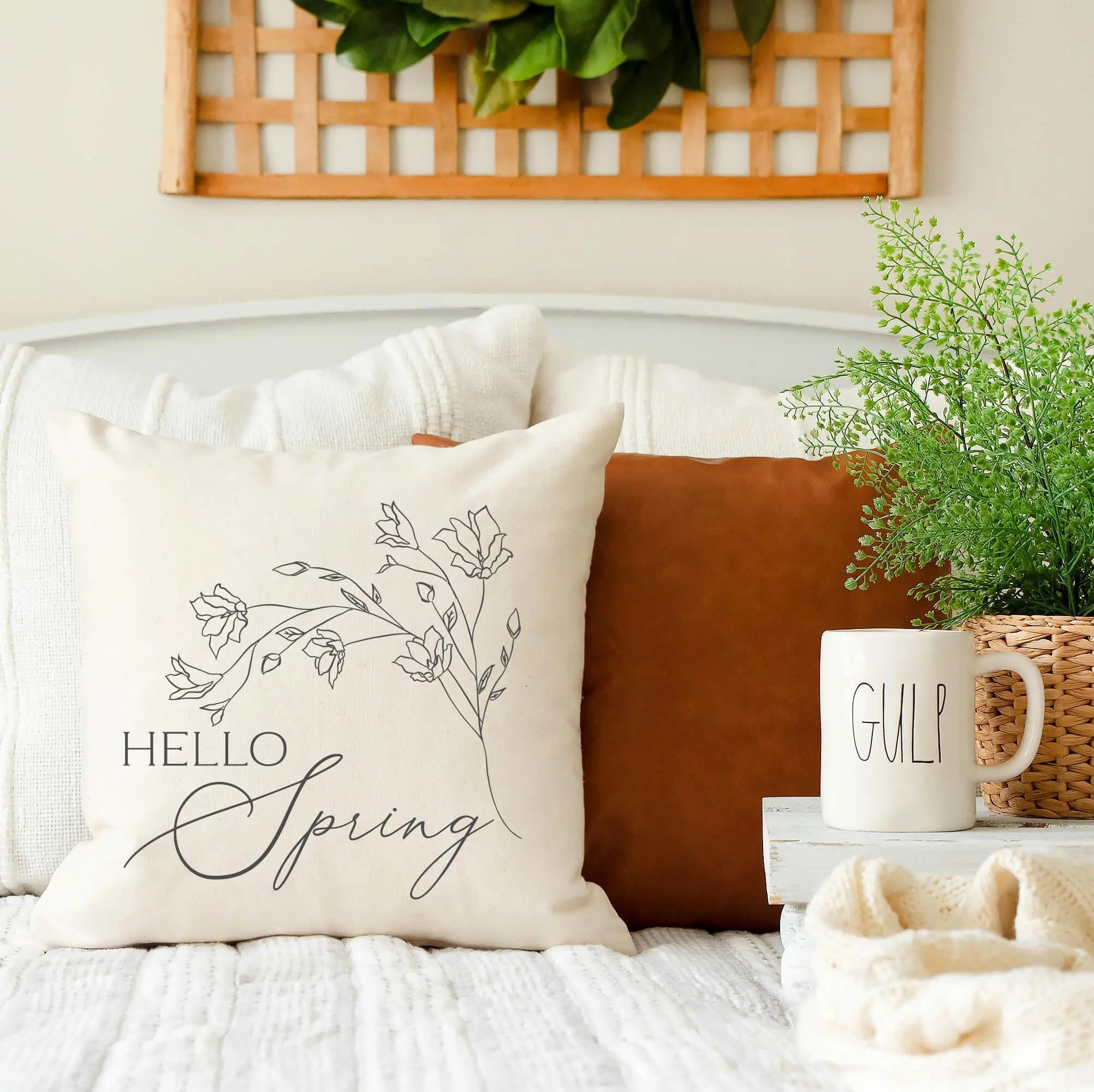 Hello Spring throw pillow with floral design, cozy farmhouse decor on bed with mug and greenery