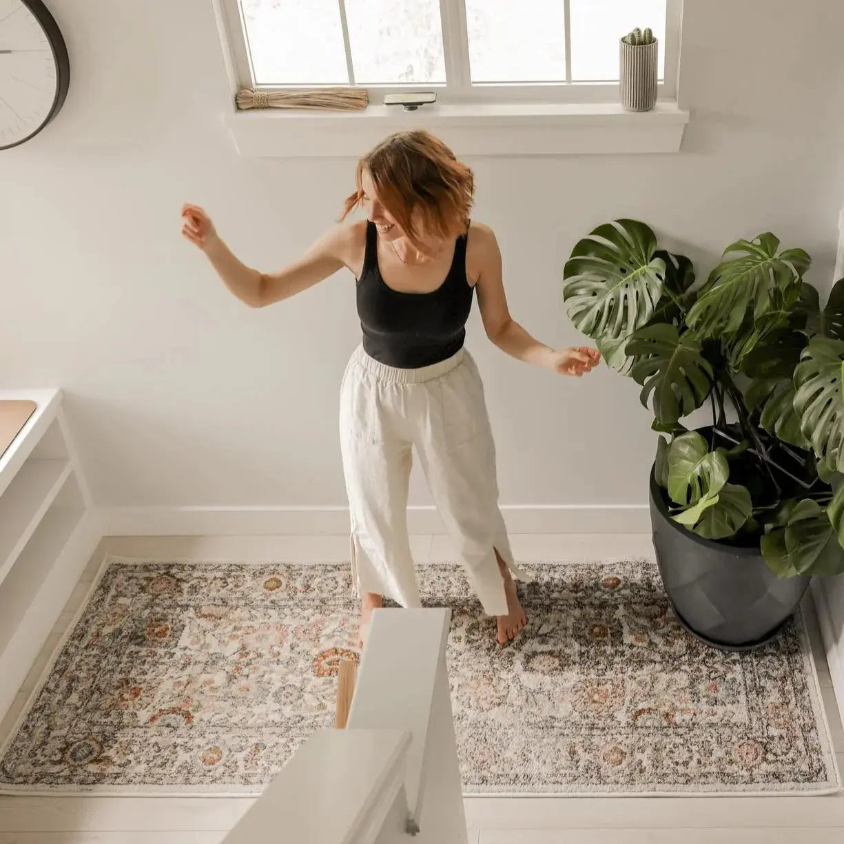 Woman dancing on cozy farmhouse-style rug with monstera plant, perfect for cottage decor and peaceful living spaces