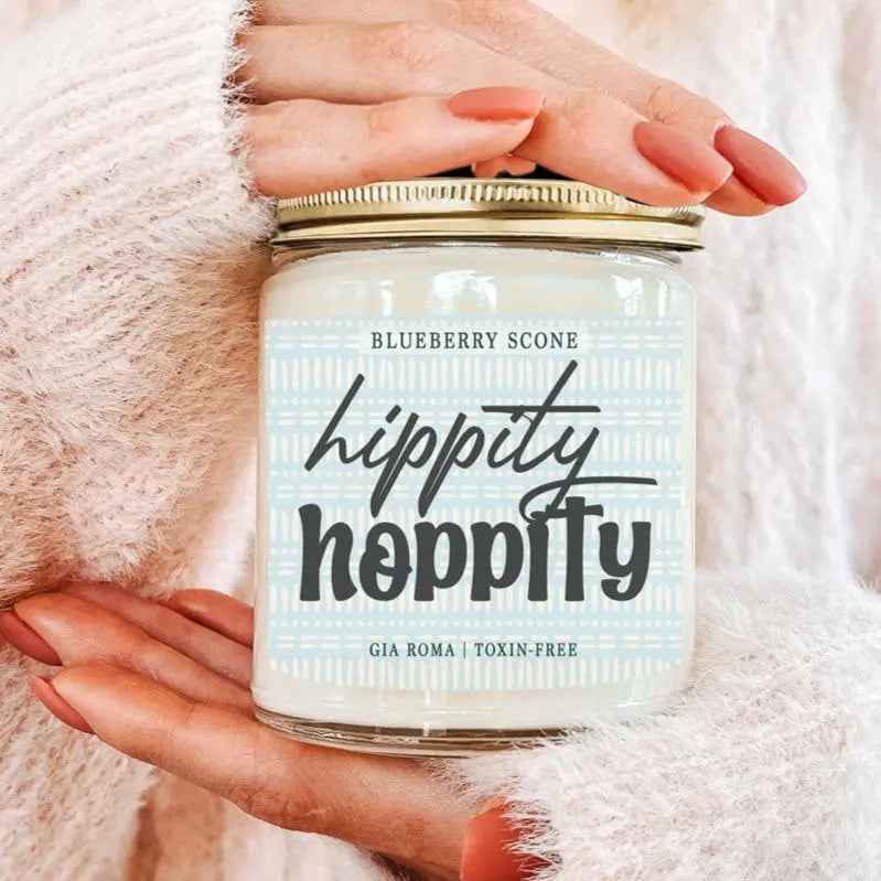 Hand holding a 'Hippity Hoppity' candle jar with a soft pink background