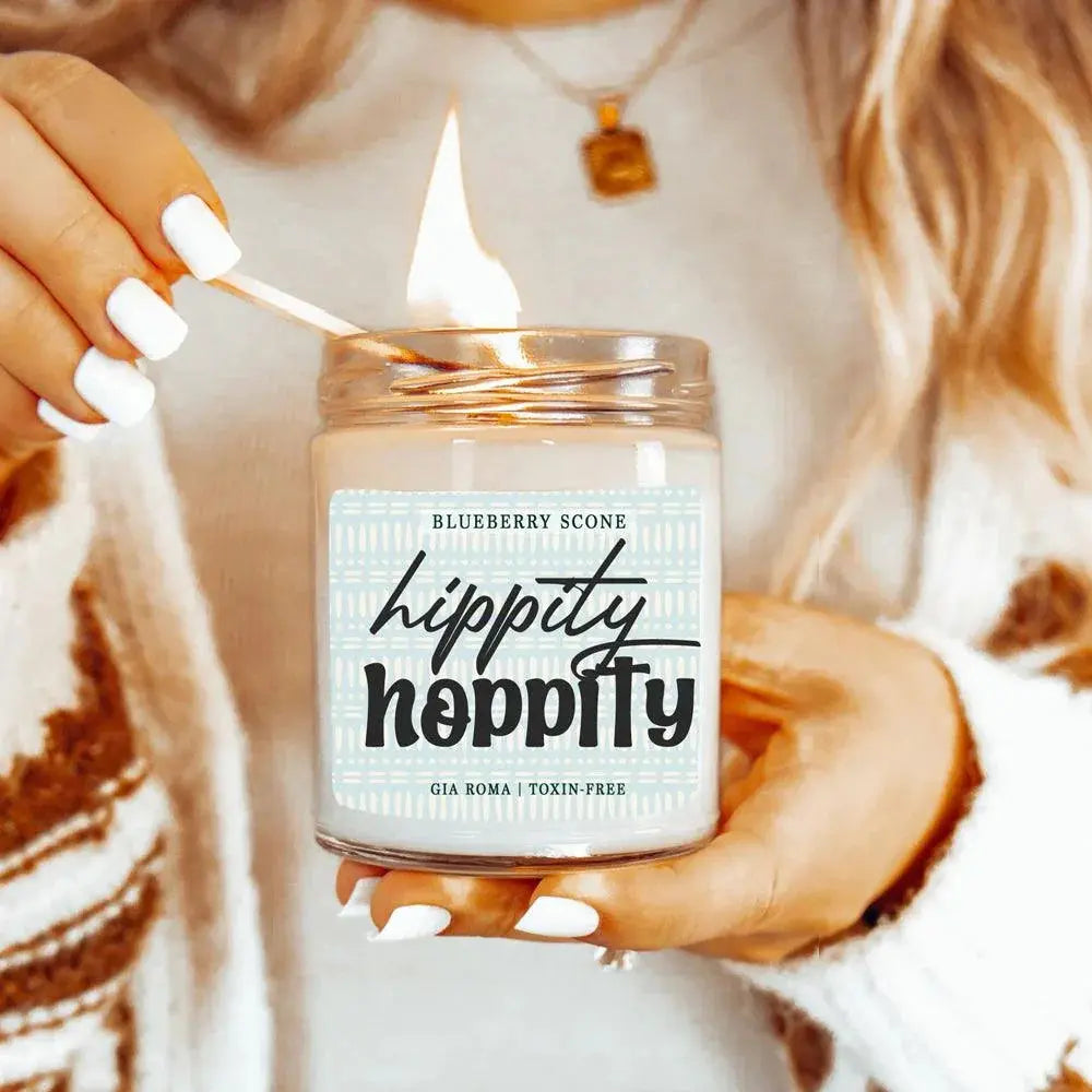 Person lighting a 'Hippity Hoppity' candle with a blueberry scone flavor.