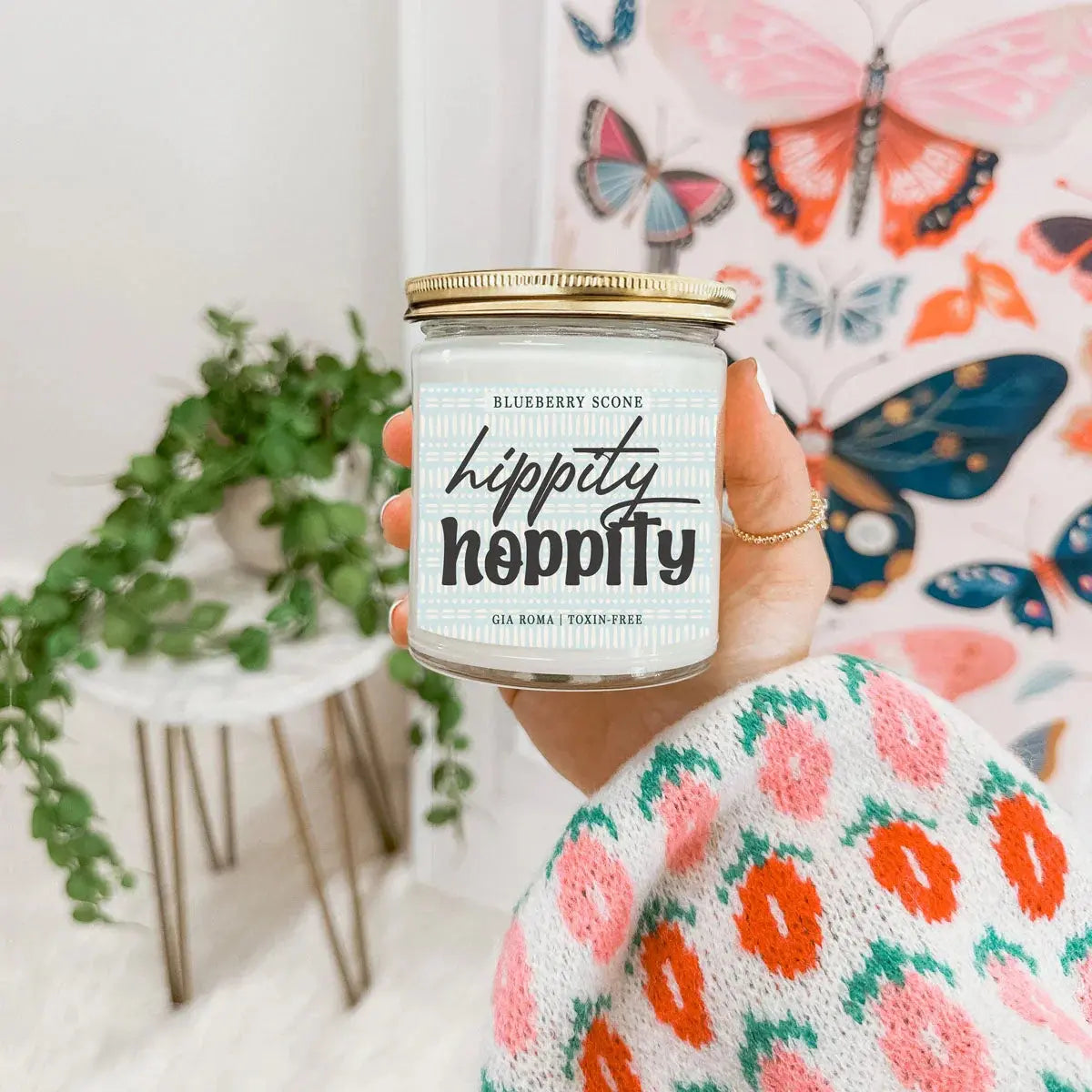 Person holding a 'hippity hippity' candle with a colorful butterfly-patterned bag in the background