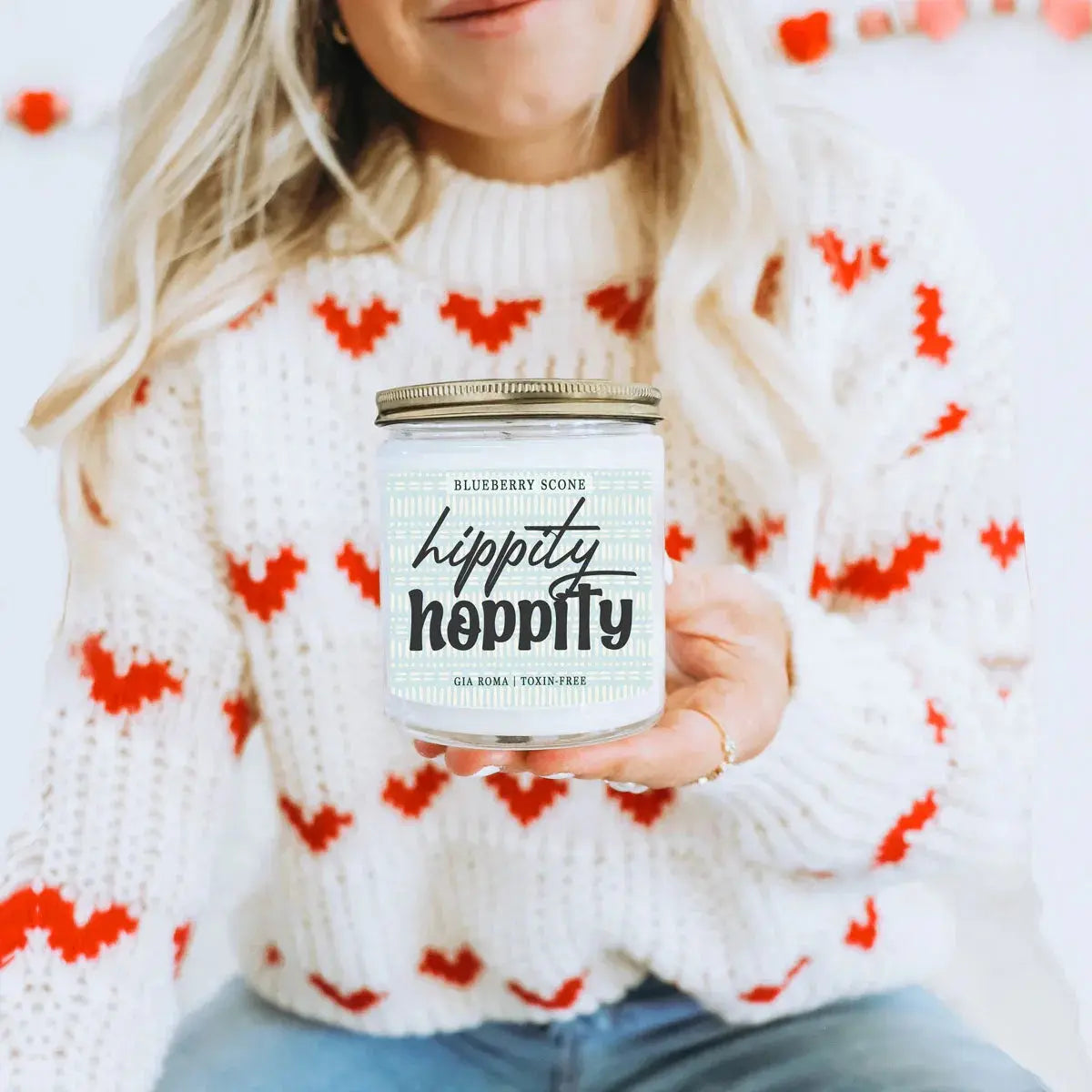 Person holding a 'hippity hippity' candle in a cozy sweater