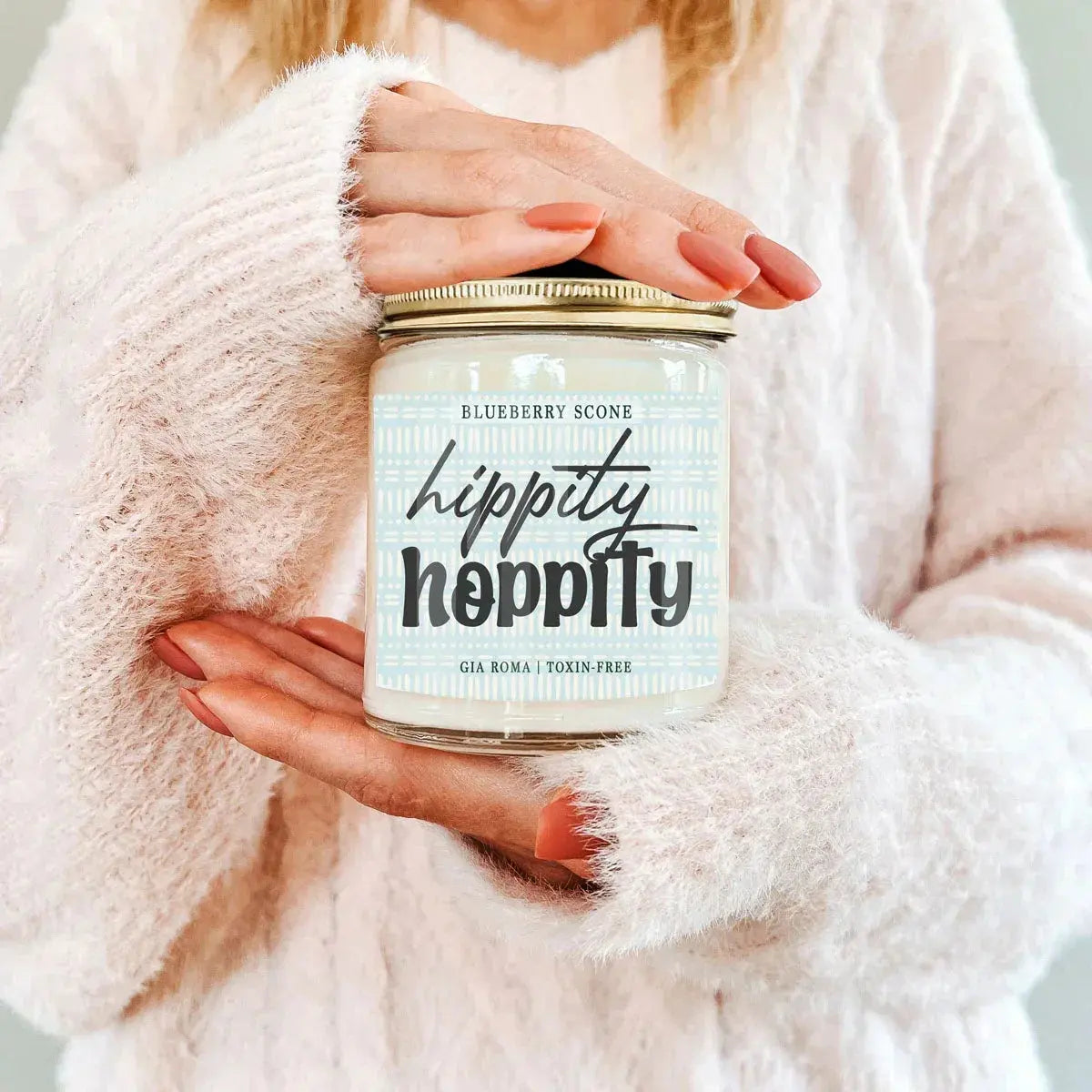 Person holding a 'hippity hoppity' candle jar with a soft pink background