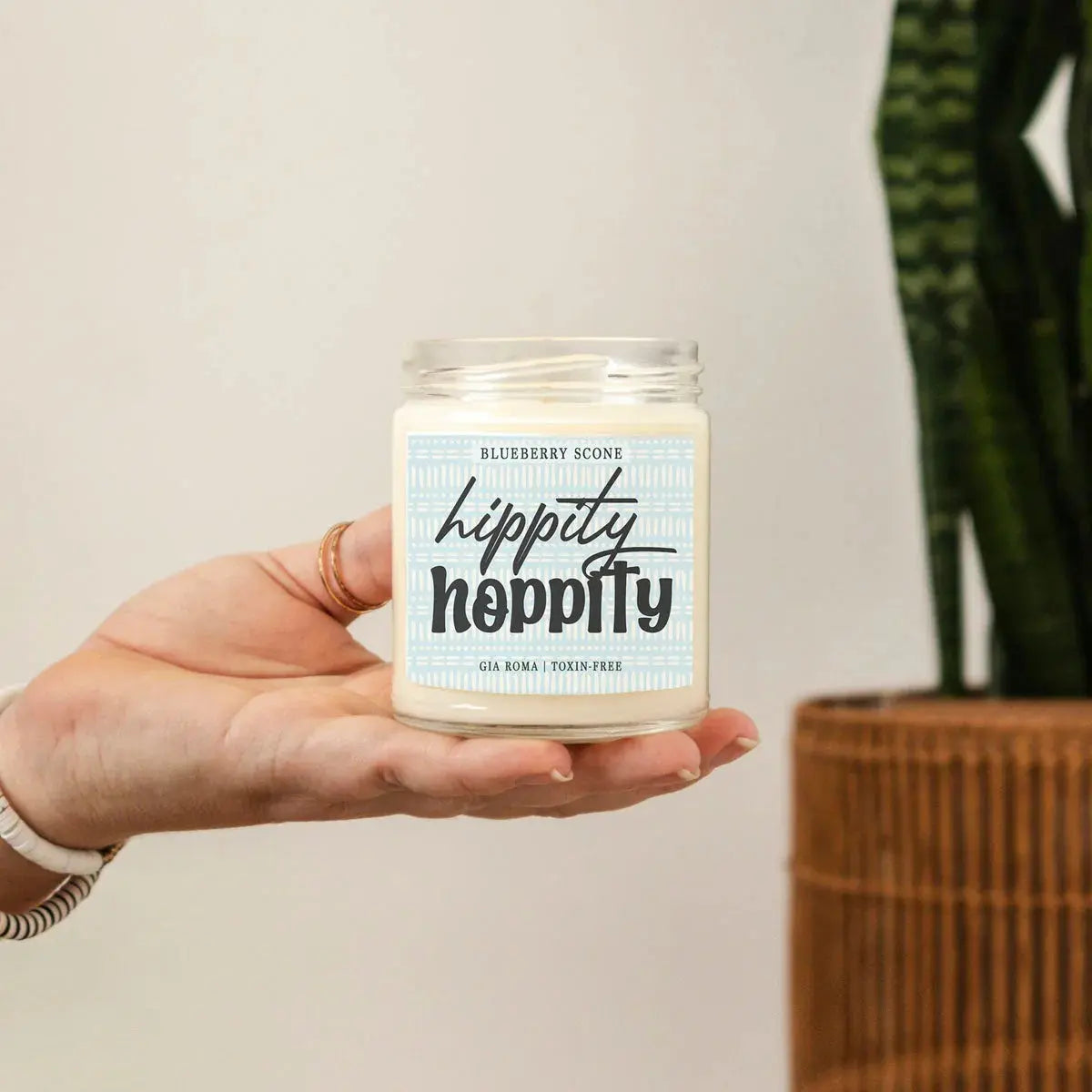 Hand holding a candle labeled 'Hippity Hoppity' with a plant in the background