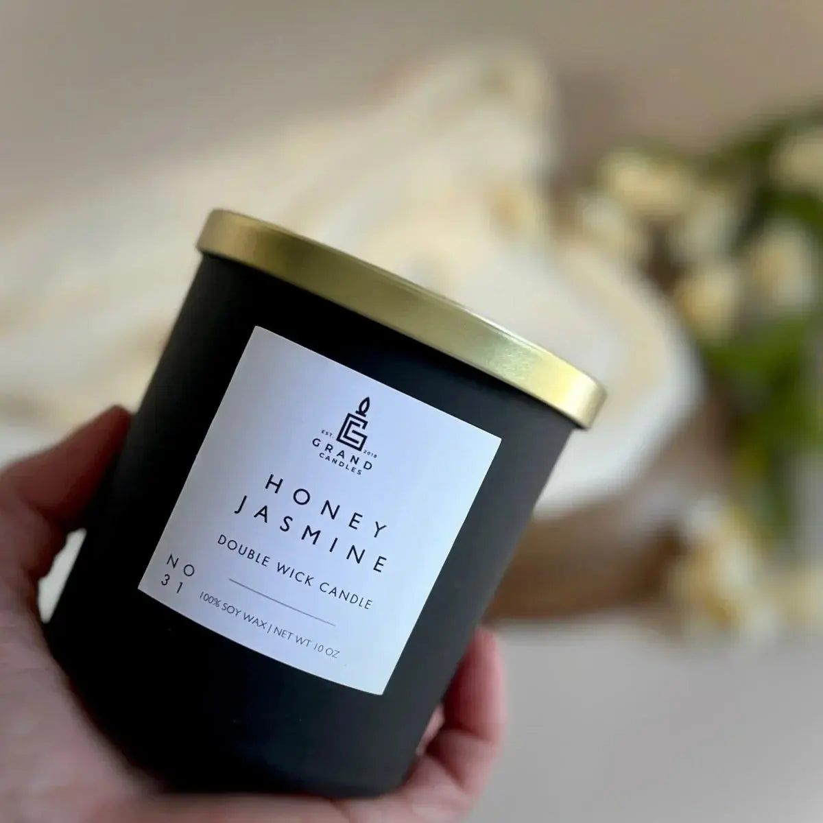 Honey Jasmine double wick soy candle in matte black jar with gold lid, held in hand for cozy home decor