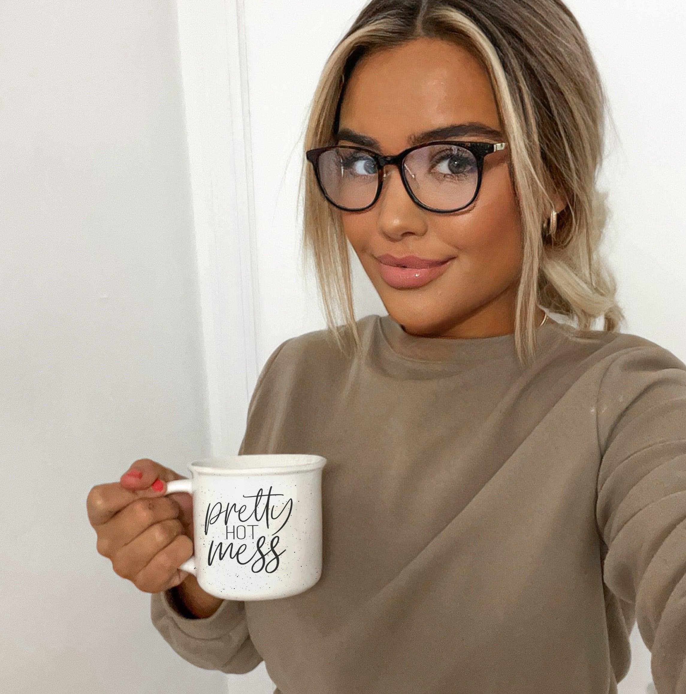 Woman holding a mug with 'pretty hot mess' text against a plain background