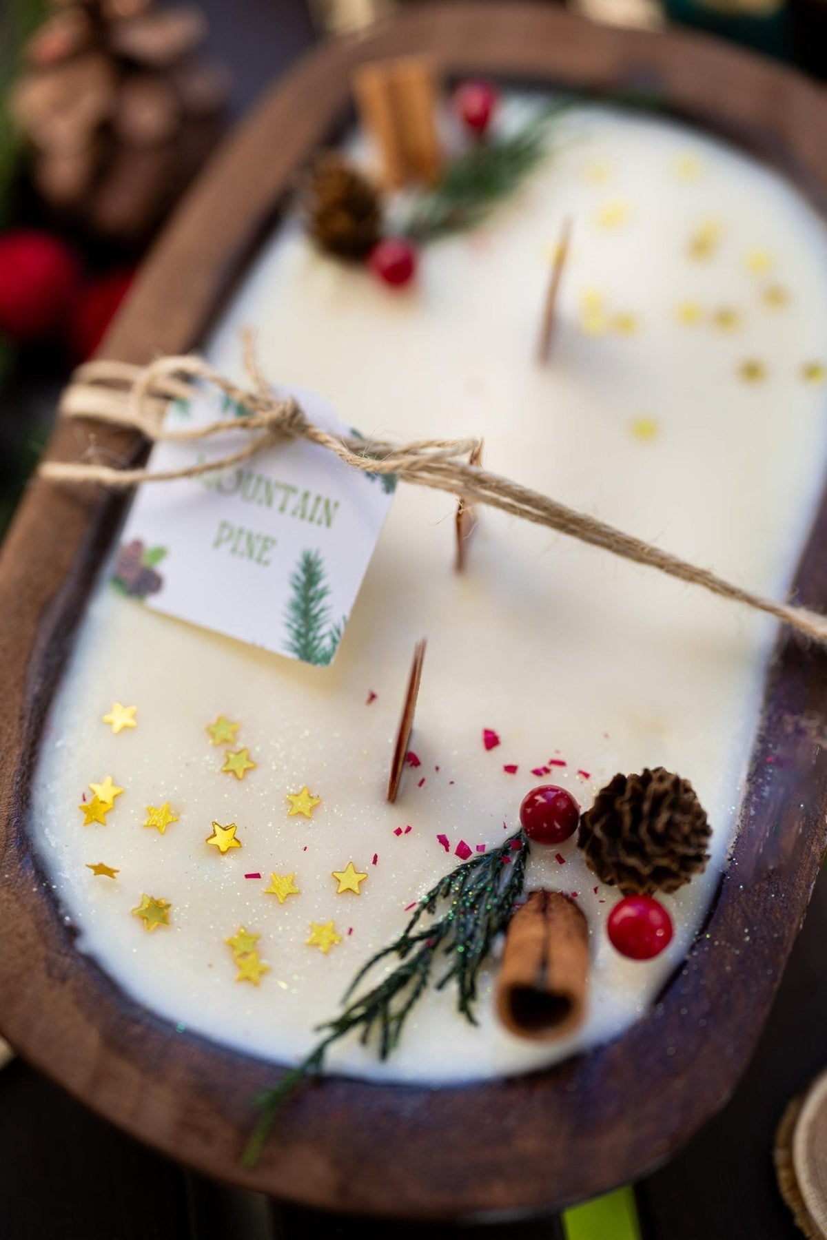 Decorative candle with pine cone, star decorations, and a tag on a wooden holder.
