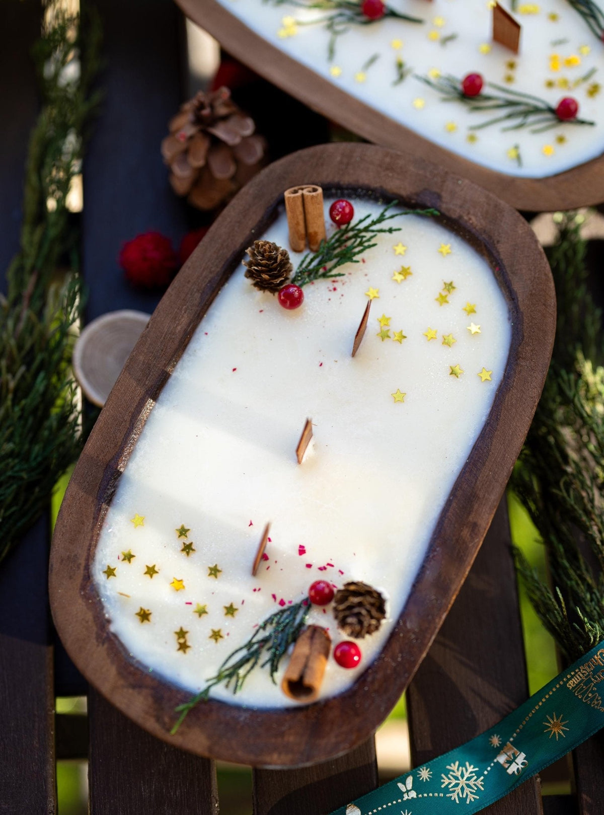 Decorative candle with cinnamon sticks, pine cones, and red berries in a wooden holder.