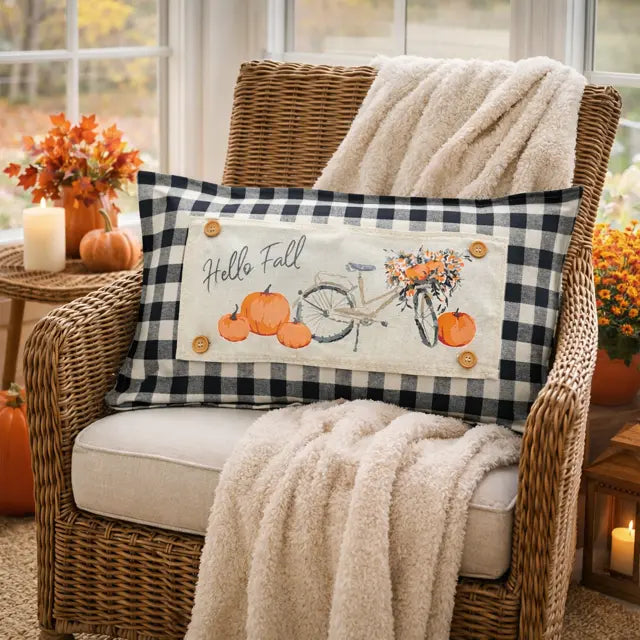Decorative pillow with 'Hello Fall' text and pumpkins on a wicker chair with a blanket.