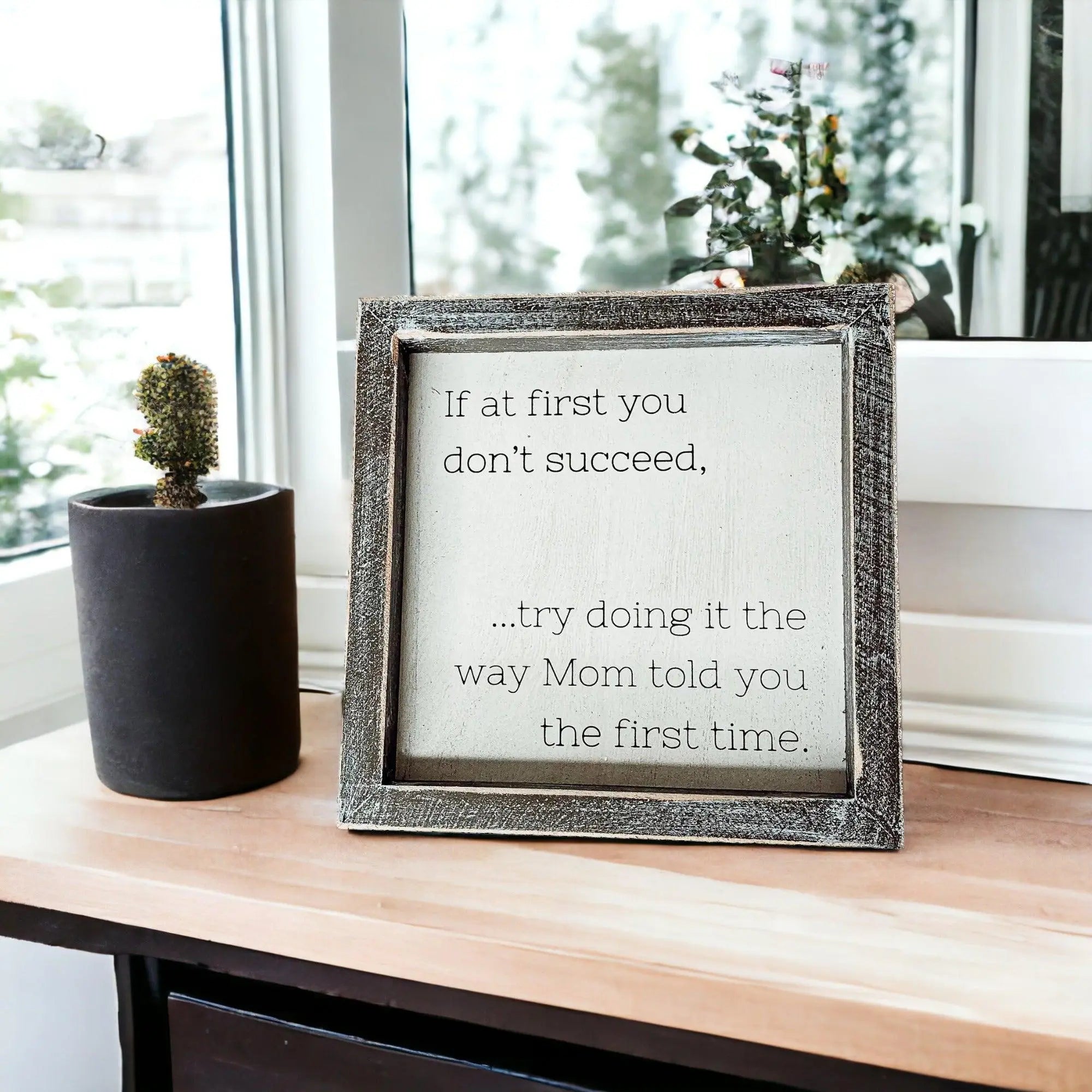 Framed motivational quote on a wooden surface with a plant in the background