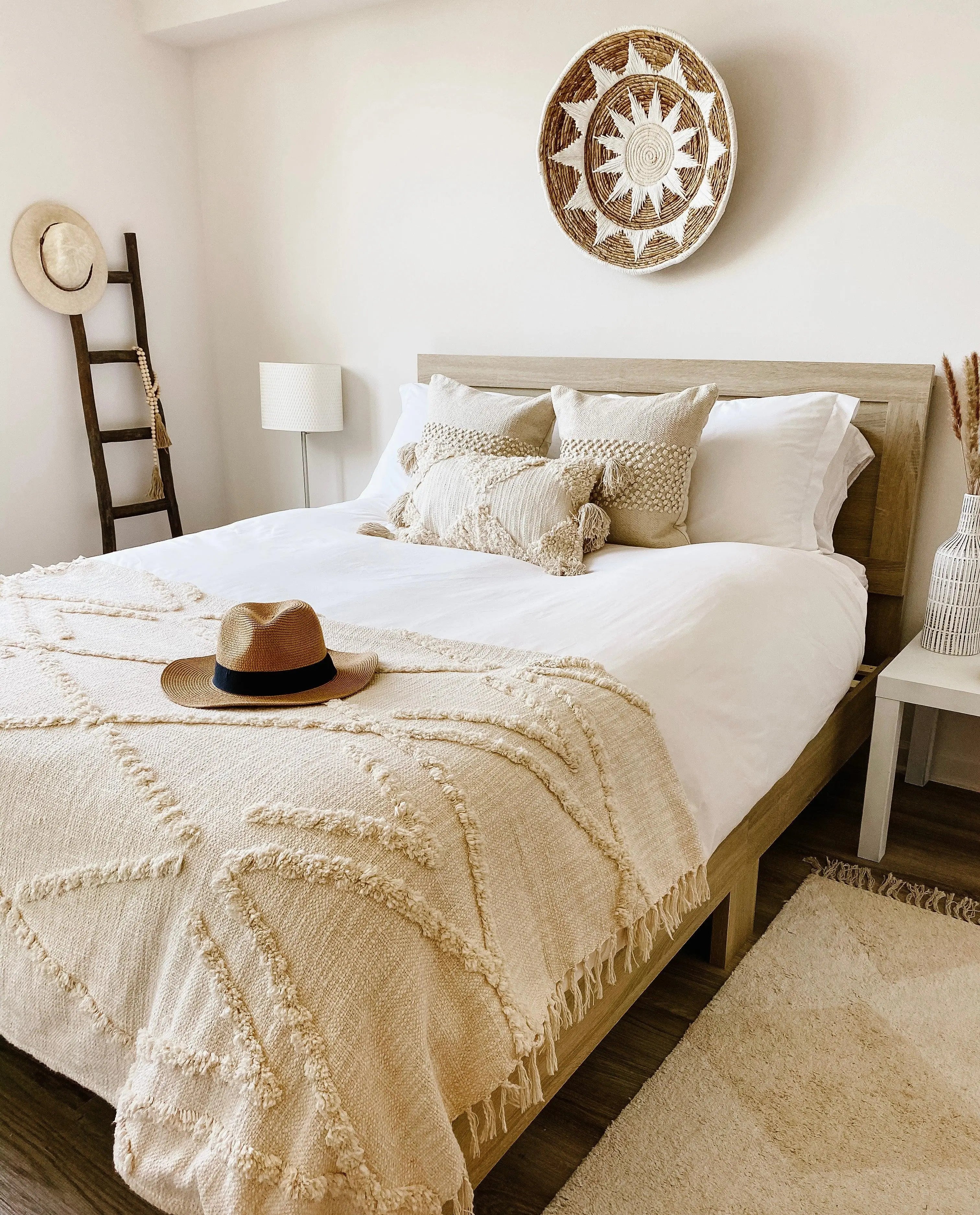Cozy farmhouse bedroom with woven sun wall decor, textured throw blanket, and straw hat on bed