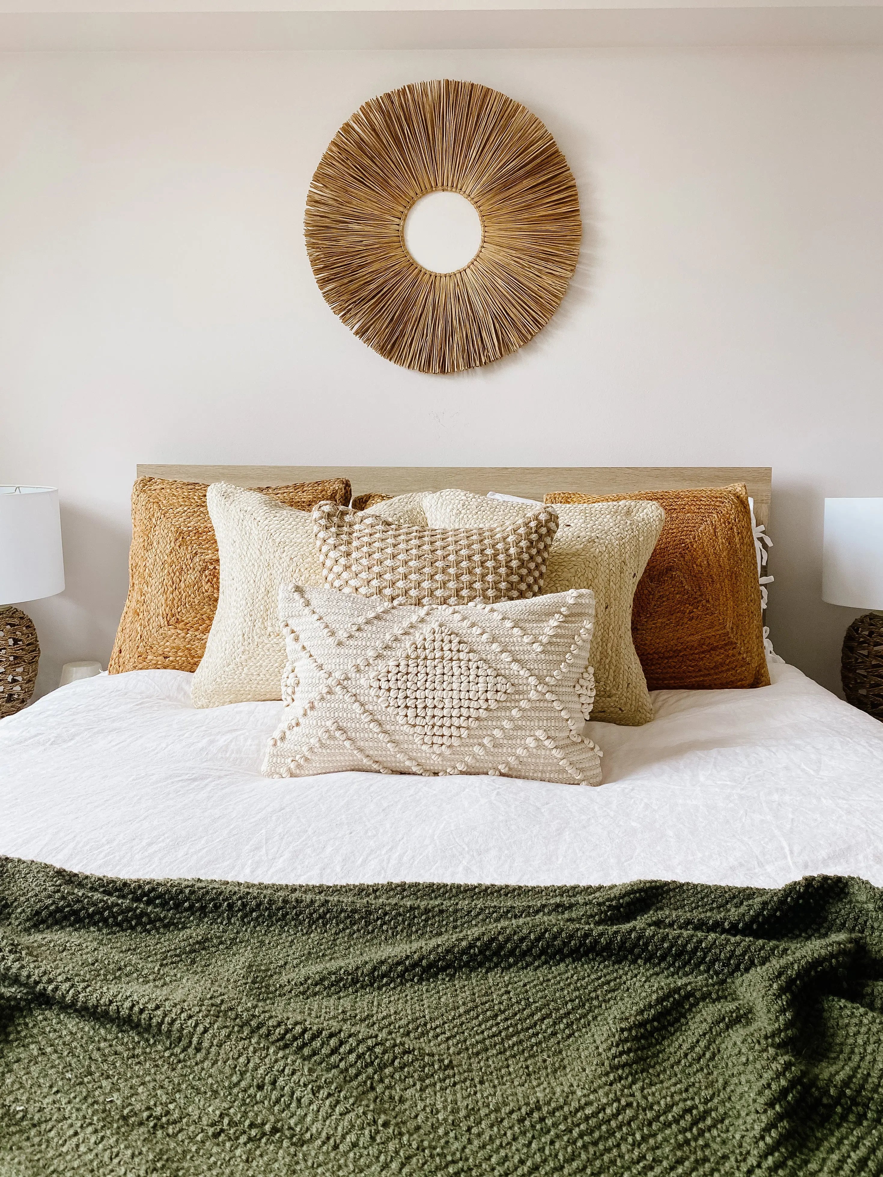 Cozy bedroom with textured throw pillows, woven wall decor, and olive green blanket for farmhouse style comfort.