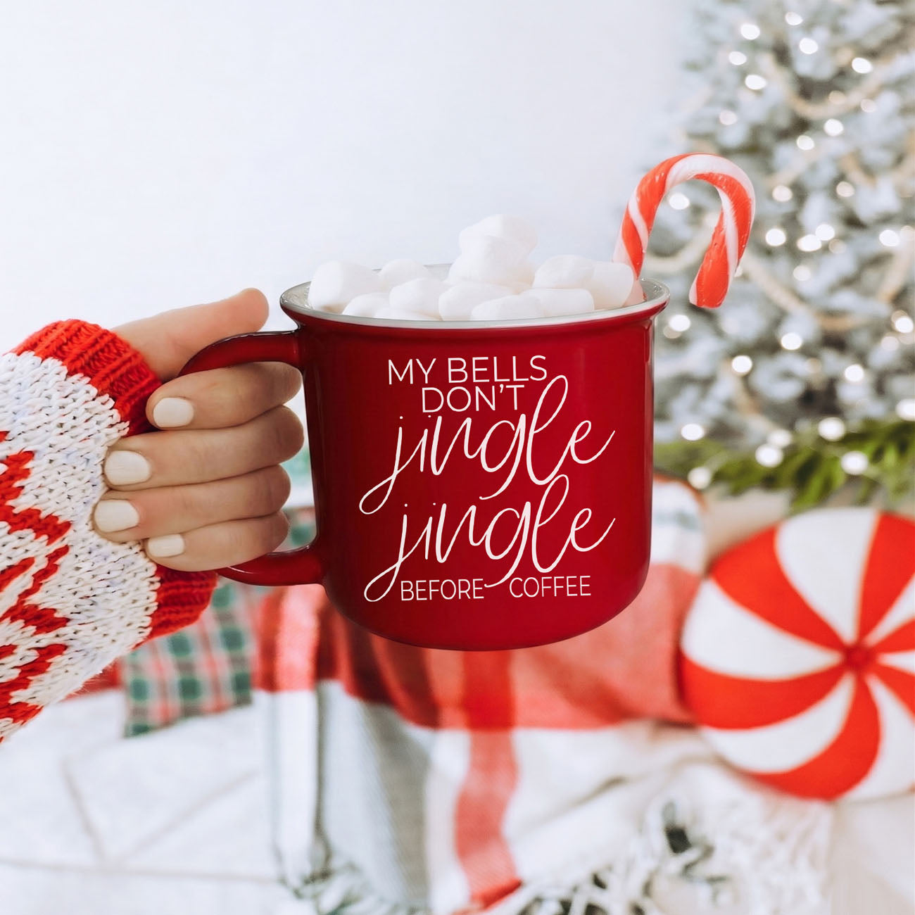 Red mug with 'My bells don't jingle jingle before coffee' text, held by a person in a festive setting with a Christmas tree.