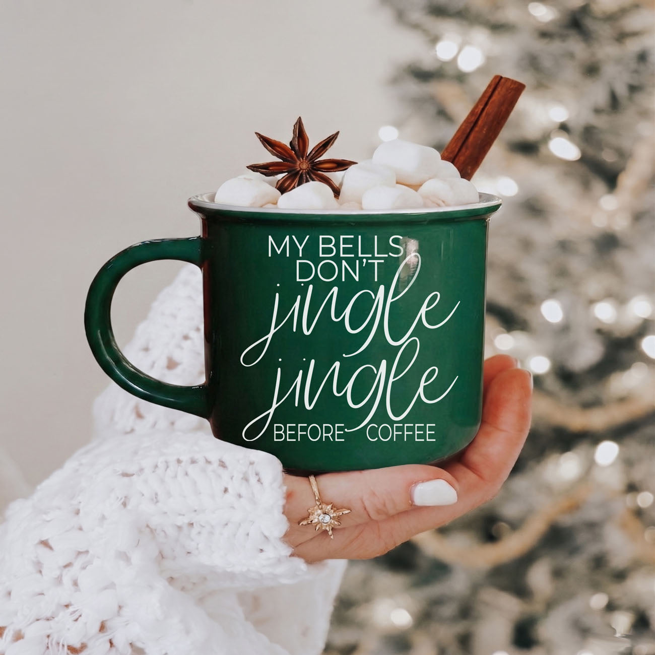 Green mug with festive text held by a person, surrounded by Christmas decorations.