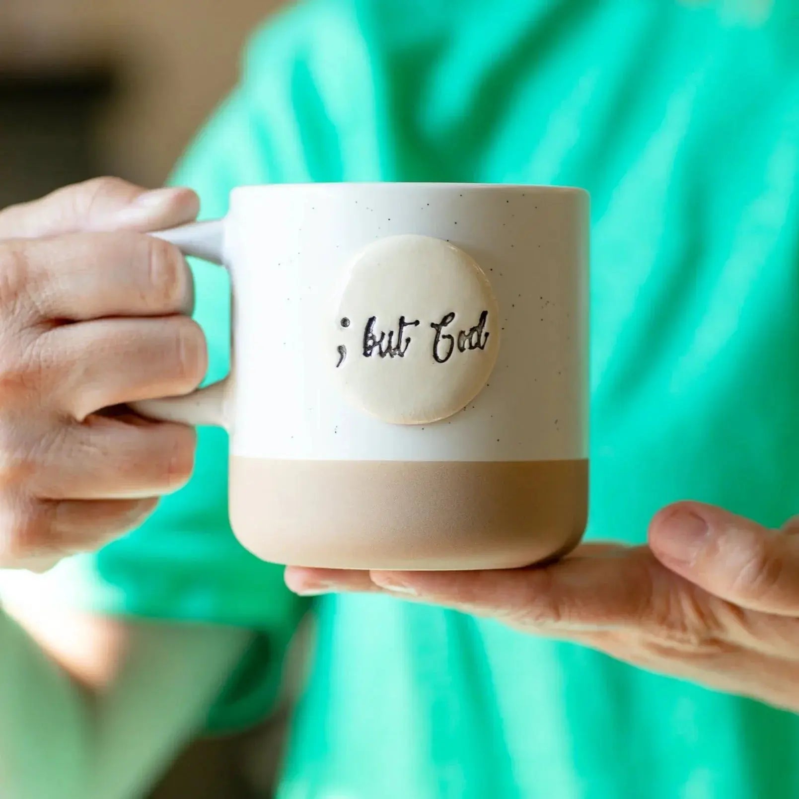 White speckled ceramic mug with '; but God' text, held in hands, cozy farmhouse decor style