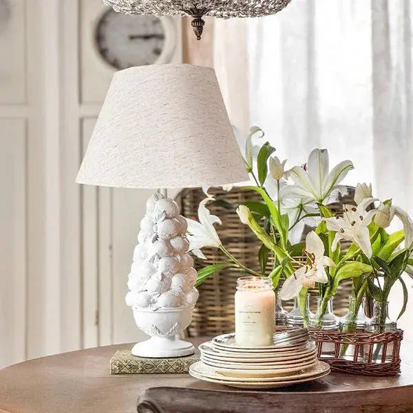 Cozy farmhouse table lamp with cotton bud base, white lilies, and candle on rustic wood table