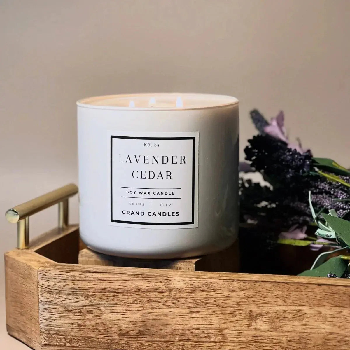 Lavender Cedar soy wax candle in white jar, lit with three wicks, styled on wooden tray with dried flowers.