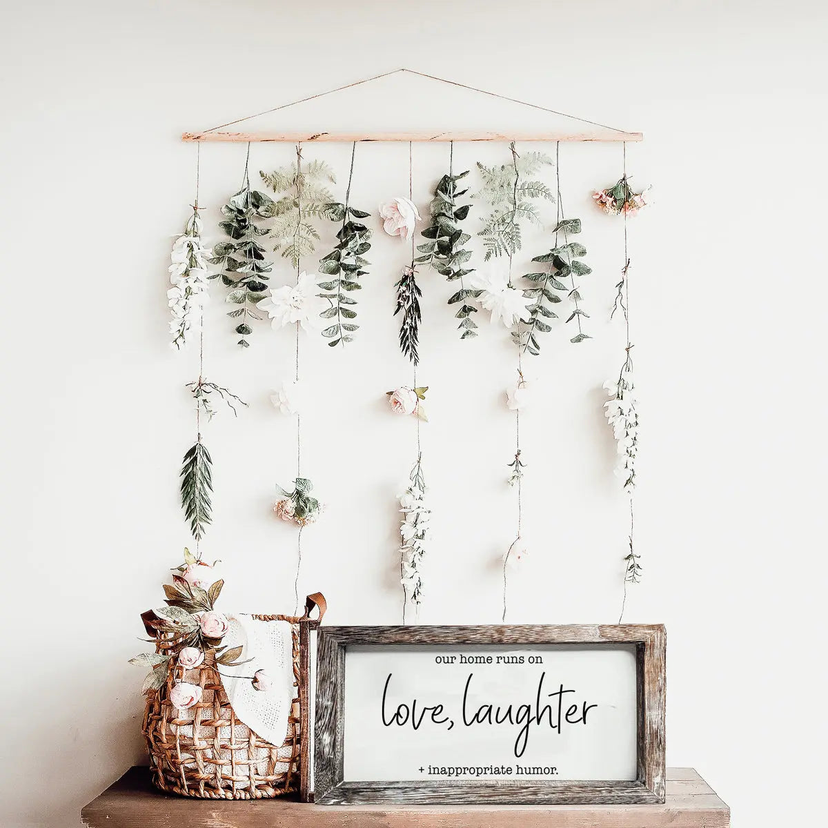 Decorative wall hanging with plants and a framed quote on a white background