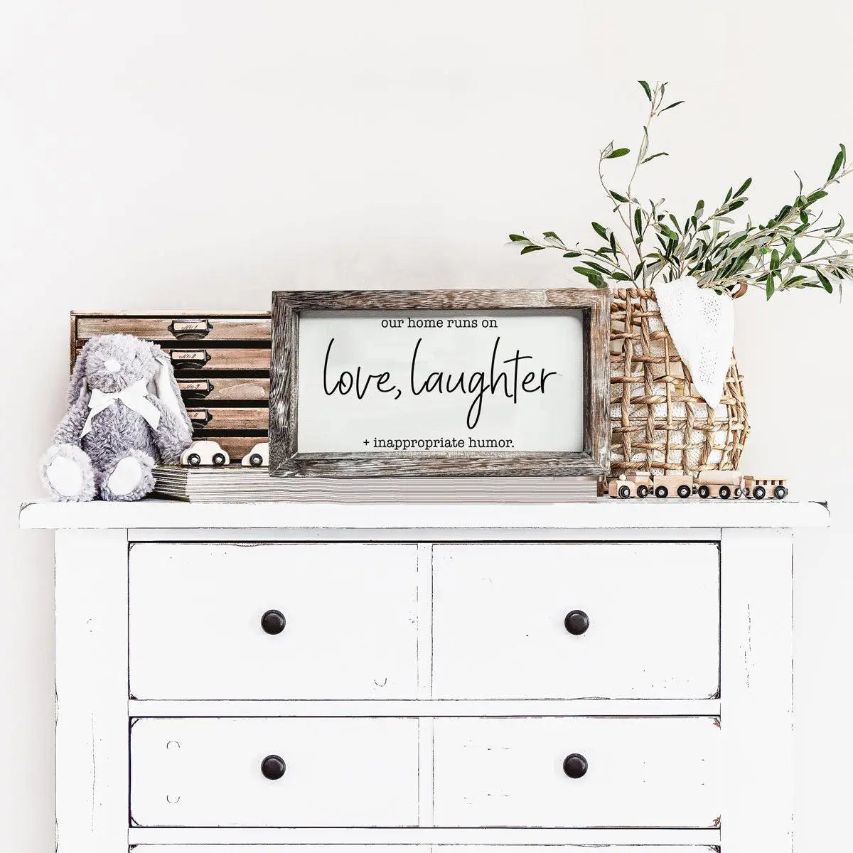 White dresser with decorative items including a framed sign, stuffed animal, and plant.