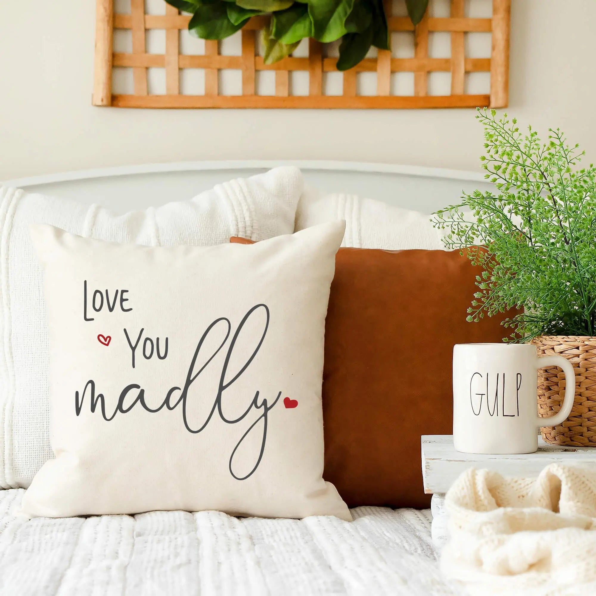 Cozy farmhouse pillow with 'Love You Madly' text, red hearts, styled on bed with rustic decor and greenery