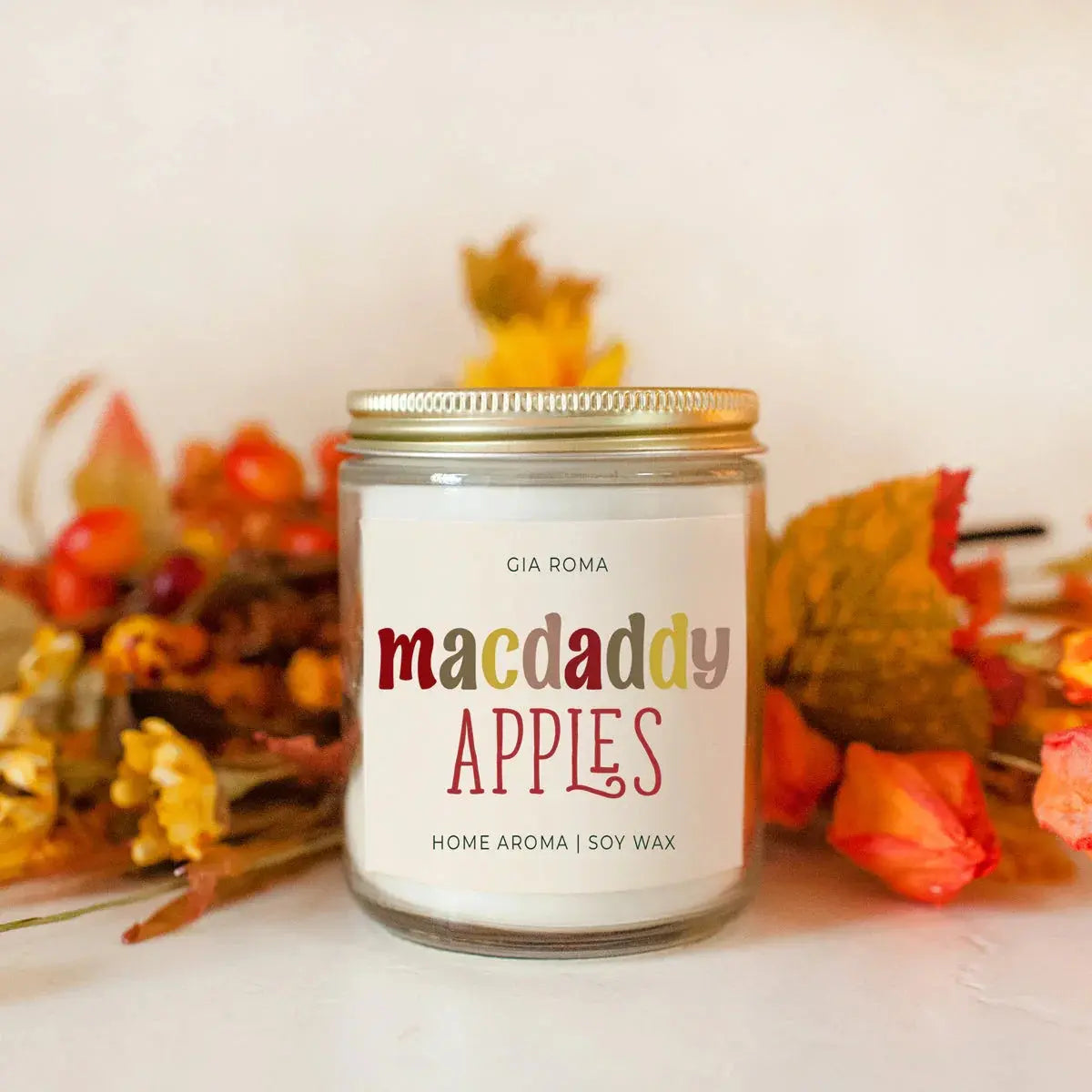 Candle labeled 'macdaddy APPLES' with autumn-themed decorations in the background