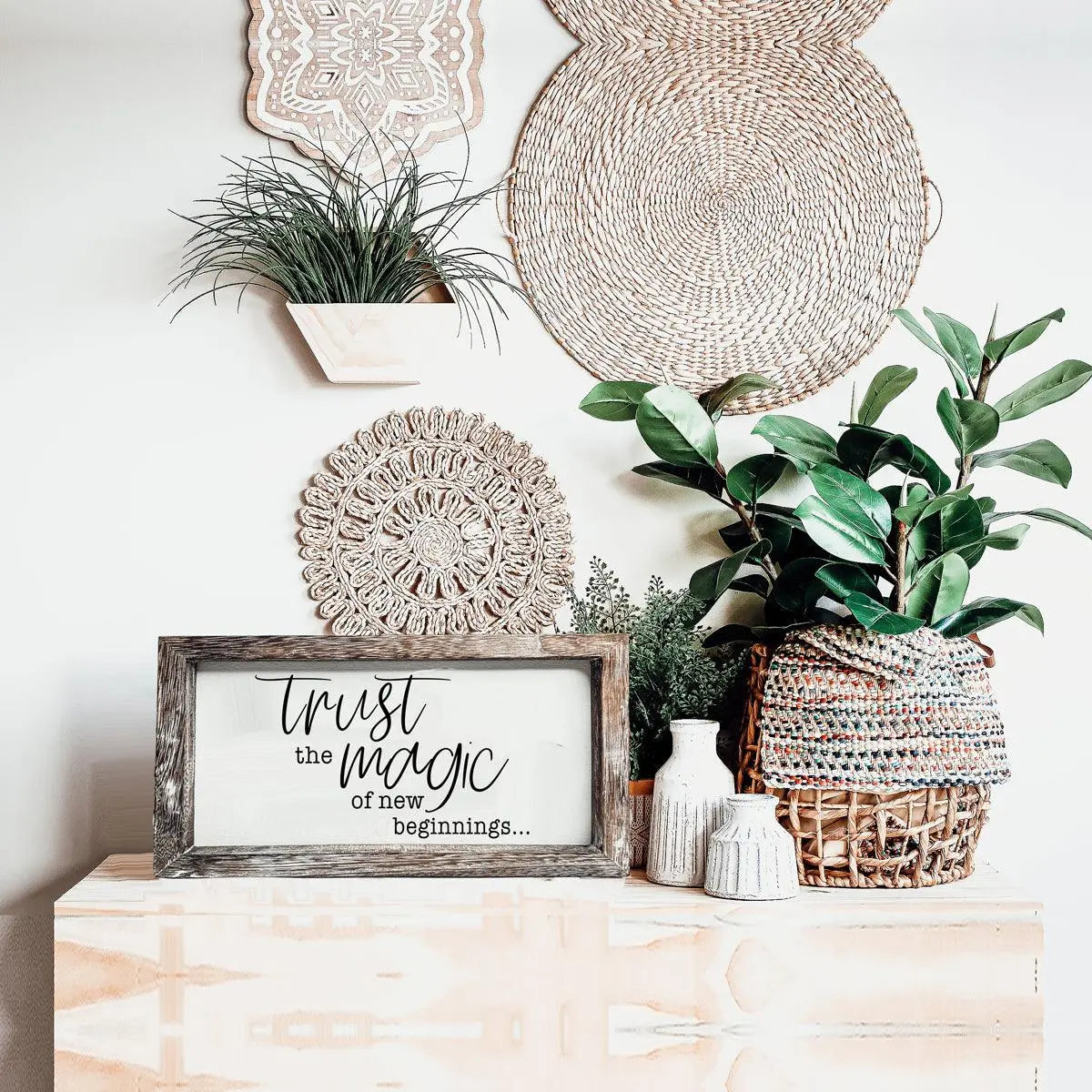 Decorative setup with plants, woven baskets, and a framed sign on a wooden surface.