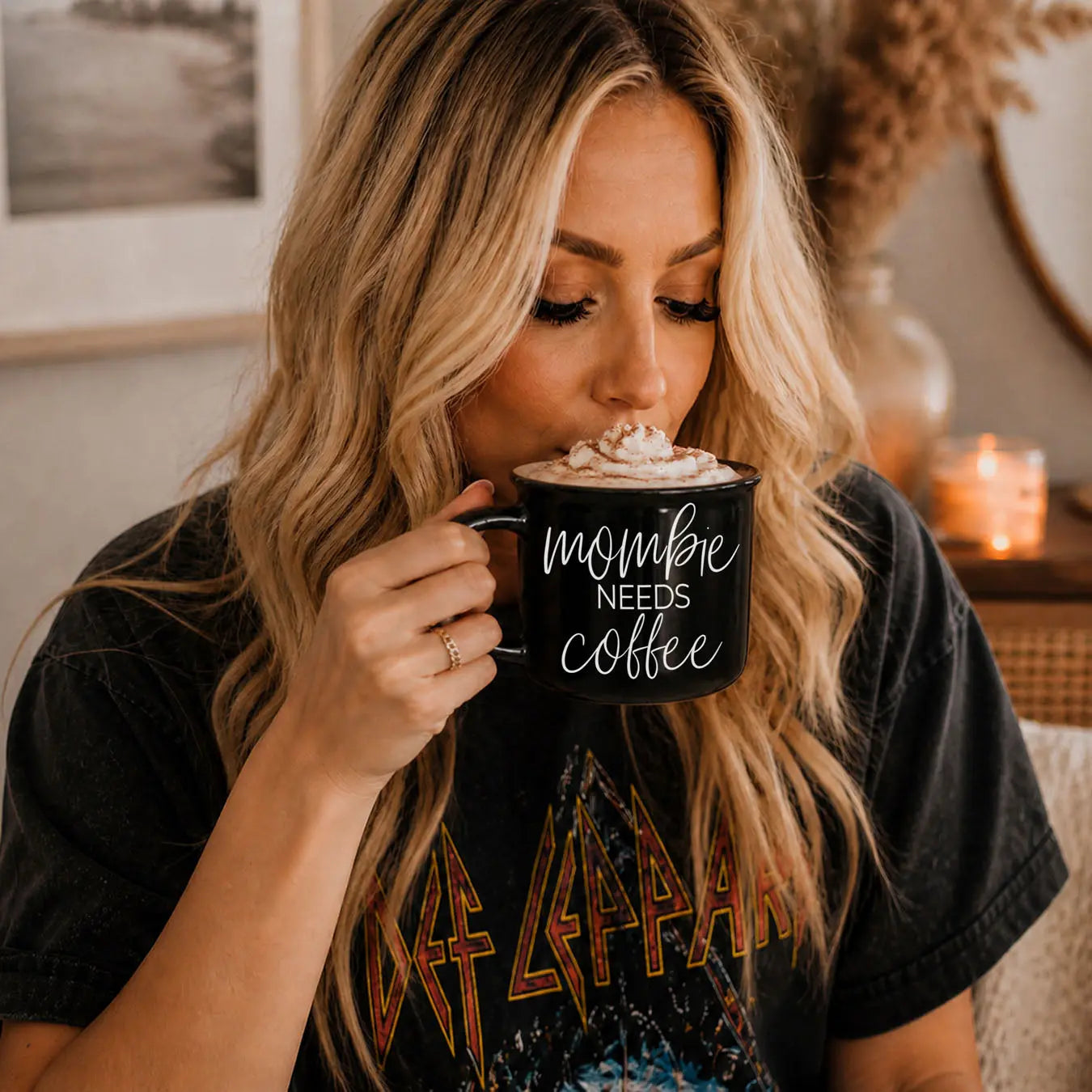 Woman drinking from a mug with 'mombe needs coffee' text in a cozy indoor setting.