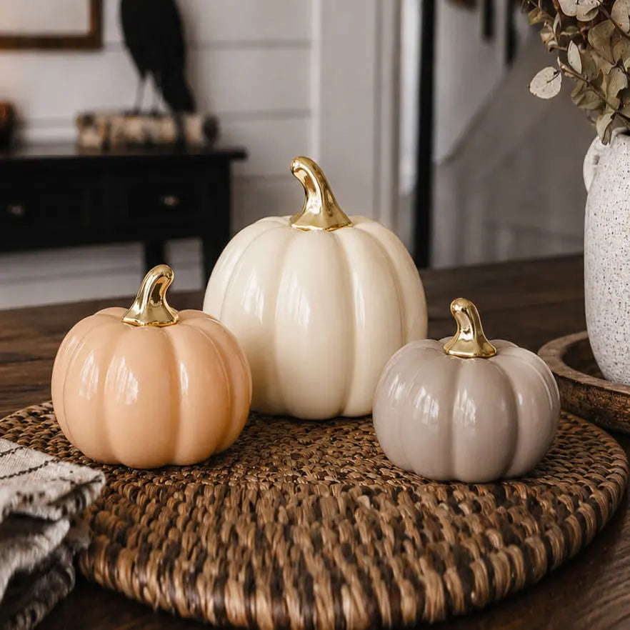 Three decorative pumpkins with gold stems on a woven surface.