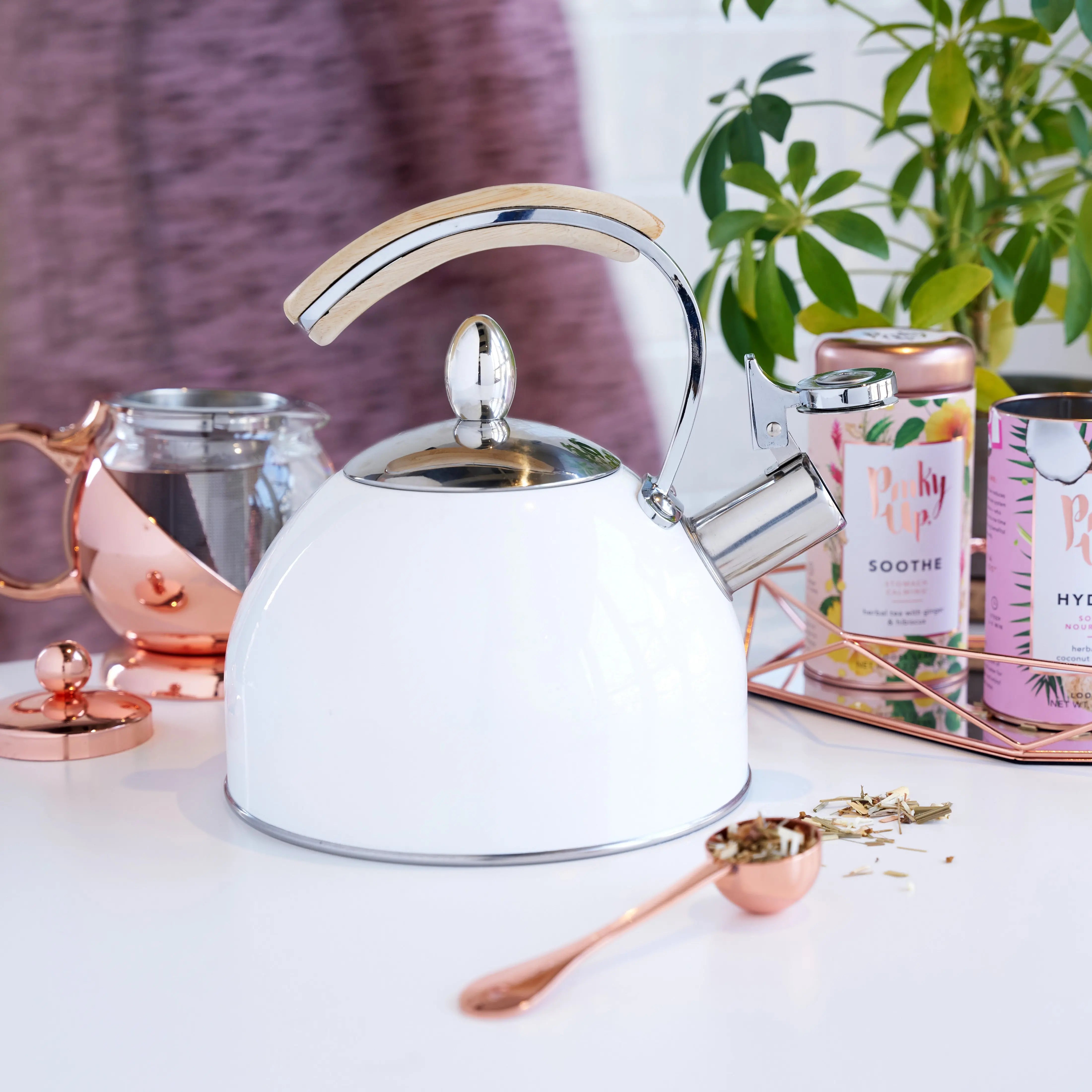White kettle with a silver handle on a table with tea-making items.