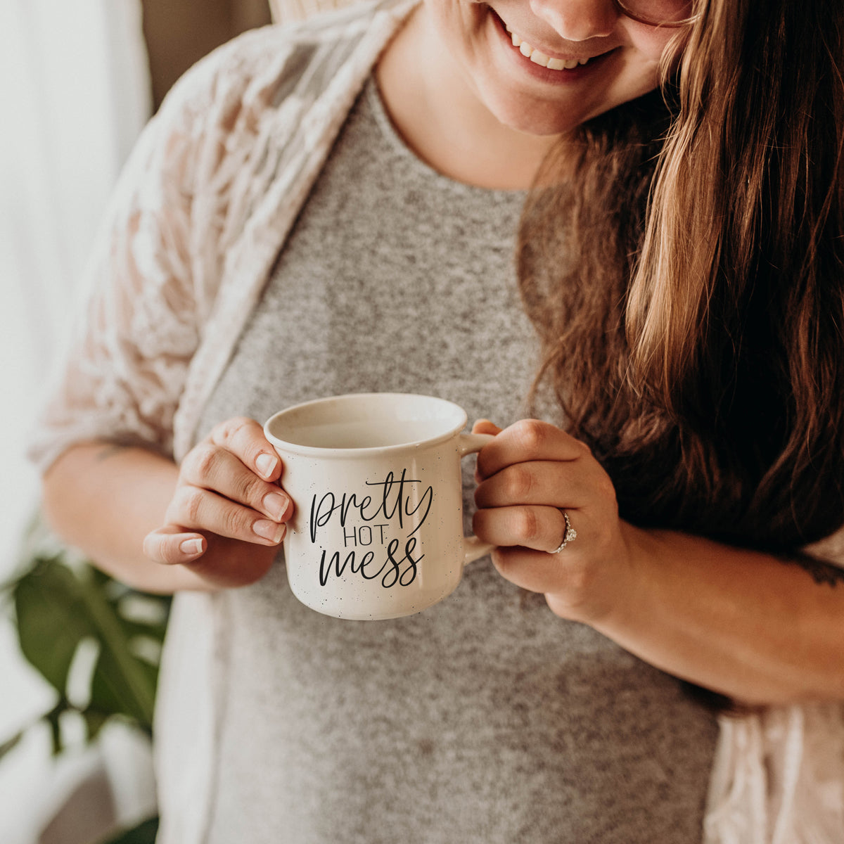 Two people hugging and holding a mug with text, with a blurred indoor background.