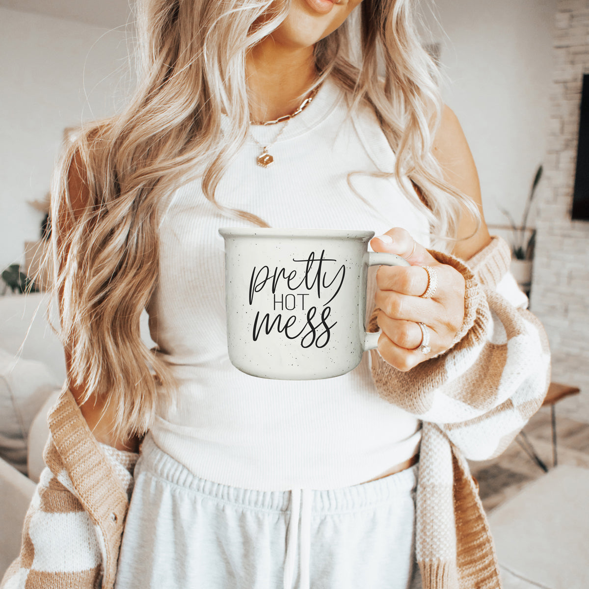 Woman holding a mug with 'pretty hot mess' text in a cozy indoor setting
