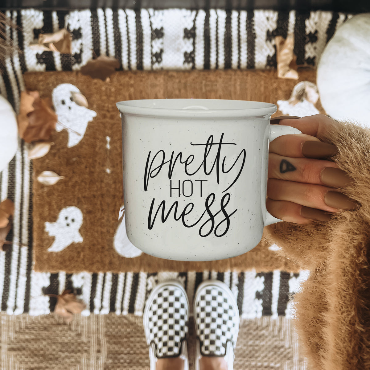 Person holding a mug with 'pretty hot mess' text against a patterned background