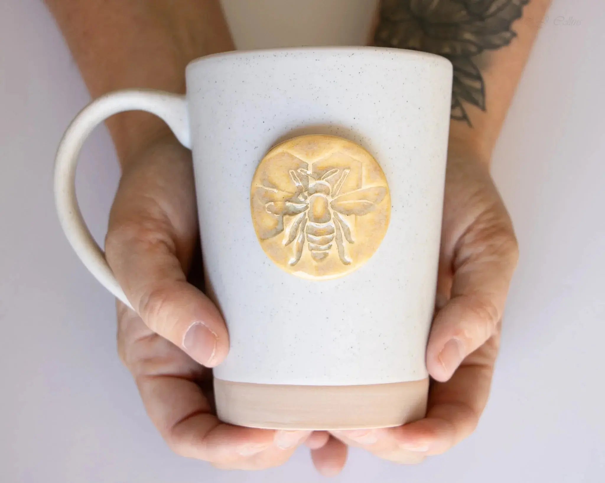Hand holding speckled ceramic mug with embossed bee design, farmhouse style home decor