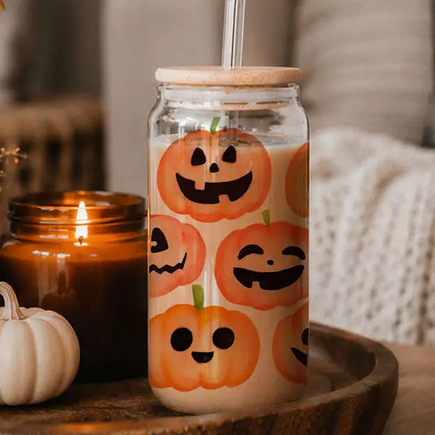Glass tumbler with pumpkin design on a wooden surface with a candle and small pumpkin.