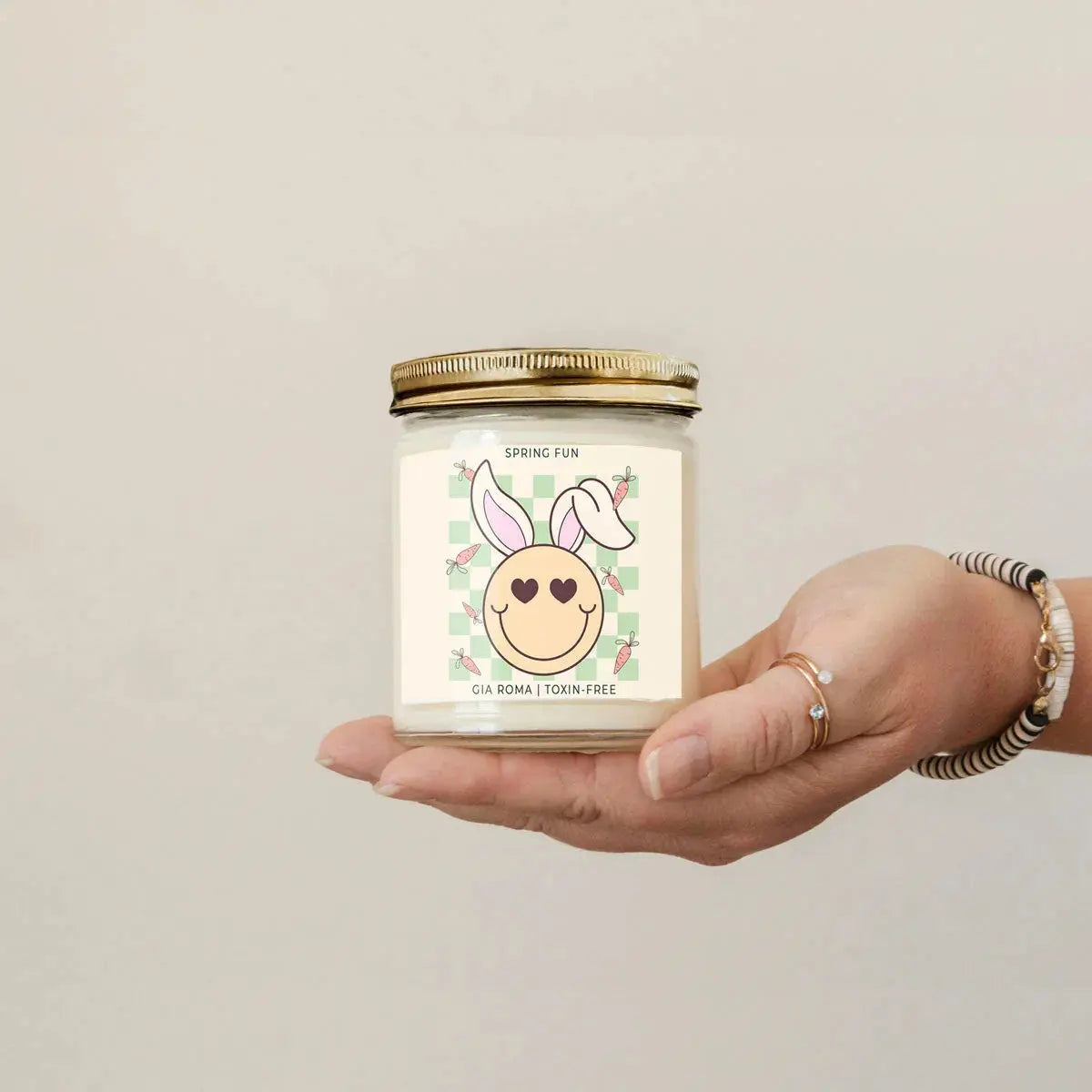 Hand holding a candle with a cute label against a plain background